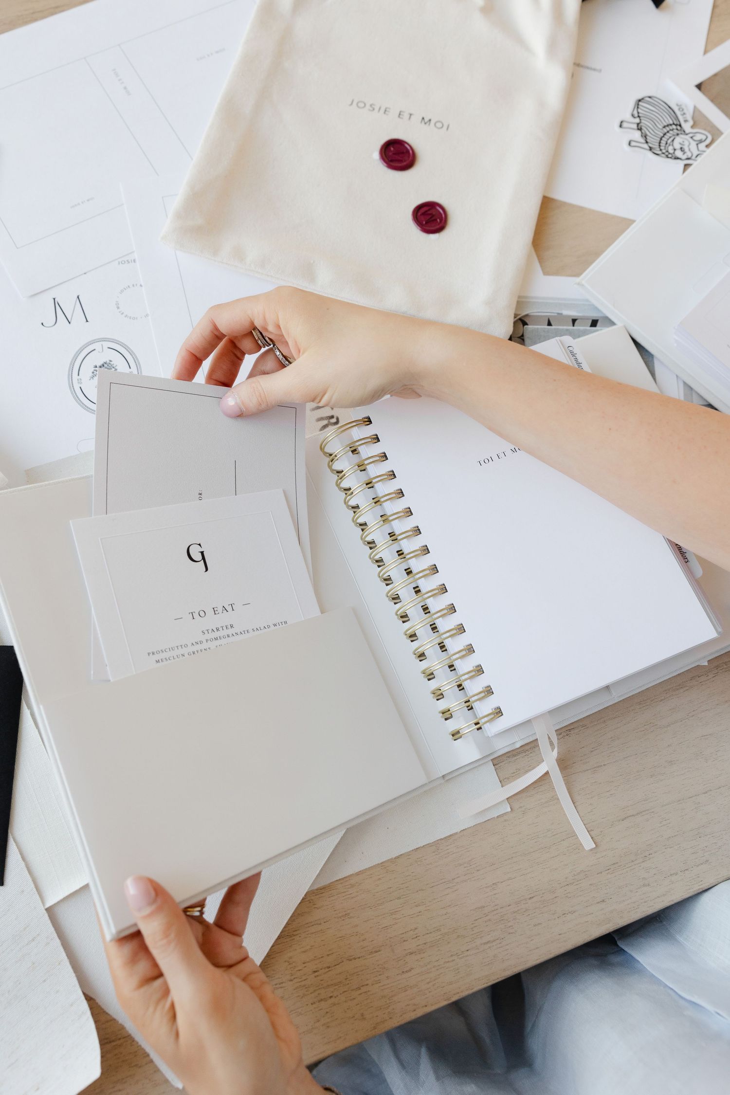White spiral notebook and papers laid out on wooden desk with red buttons and fabric bag.