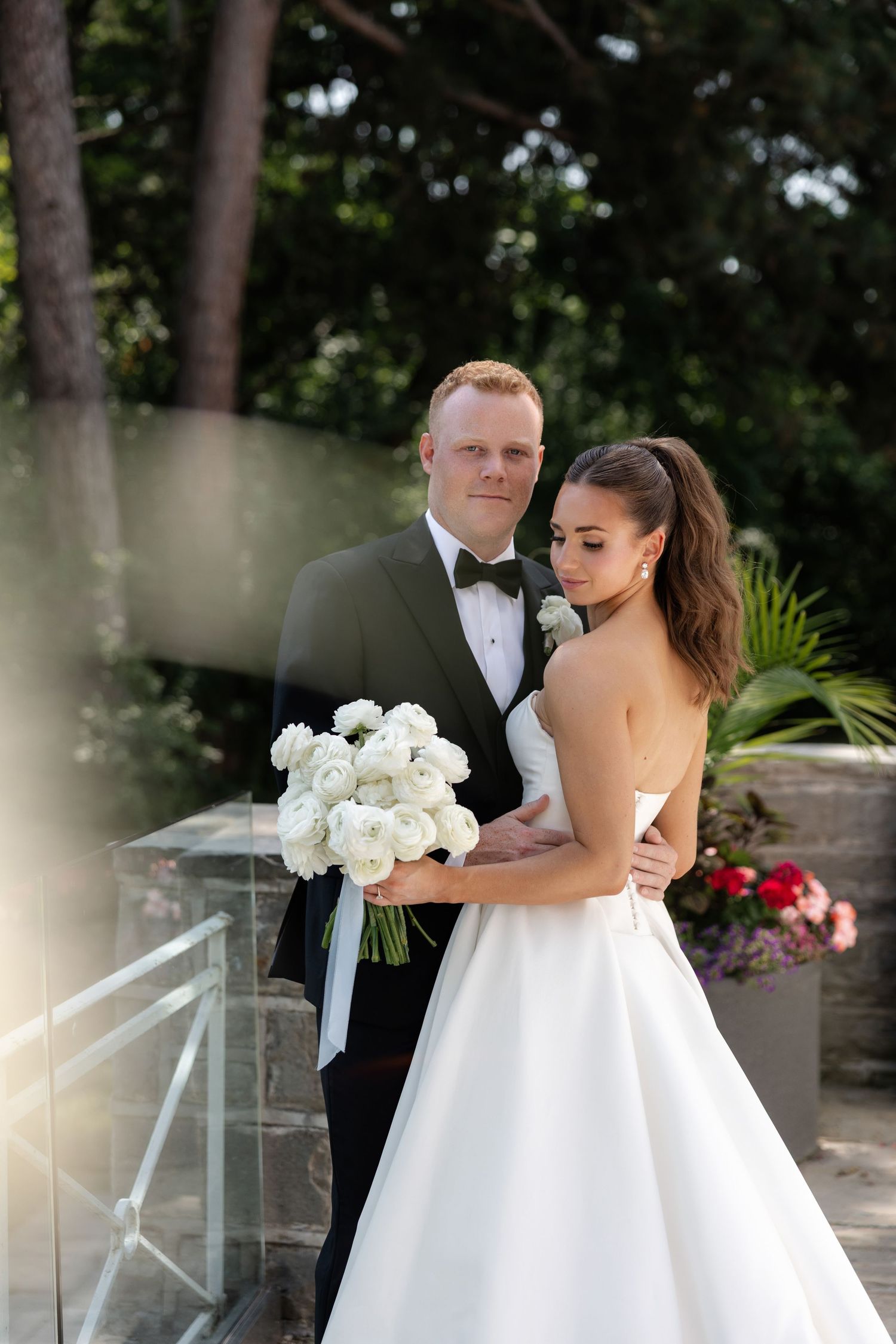 Wedding couple posing outdoors with white rose bouquet against natural garden backdrop.