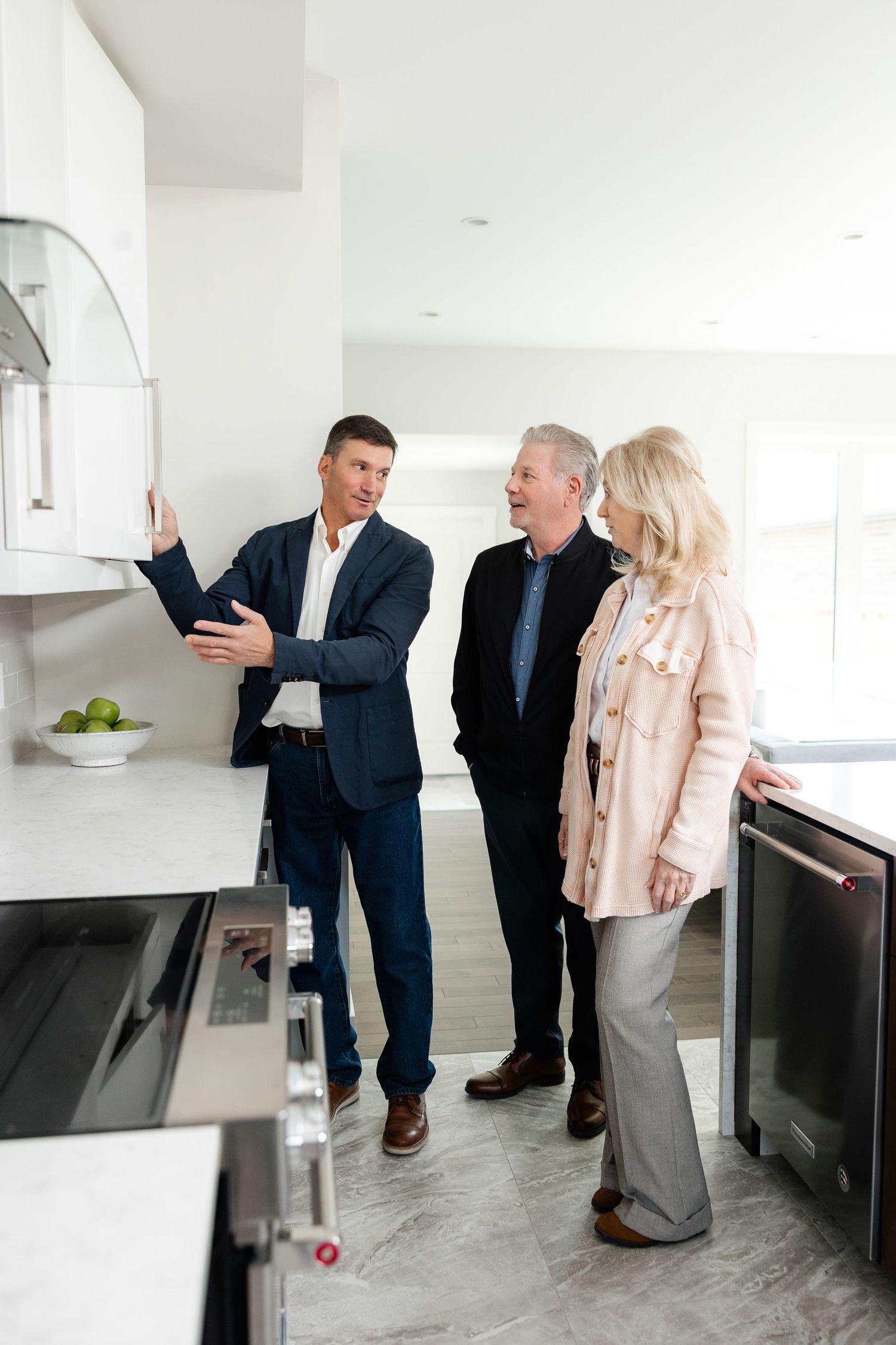 Real estate agents showing potential buyers features of a modern white kitchen during property viewing.