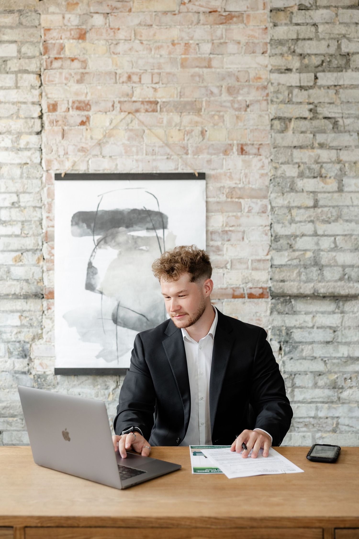 Professional working on laptop in modern office with exposed brick walls.