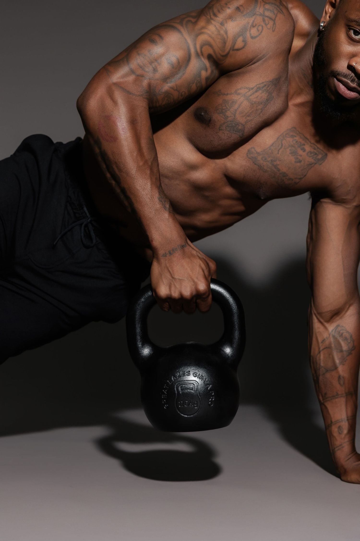 Muscular torso and arms performing plank position with kettlebell support.