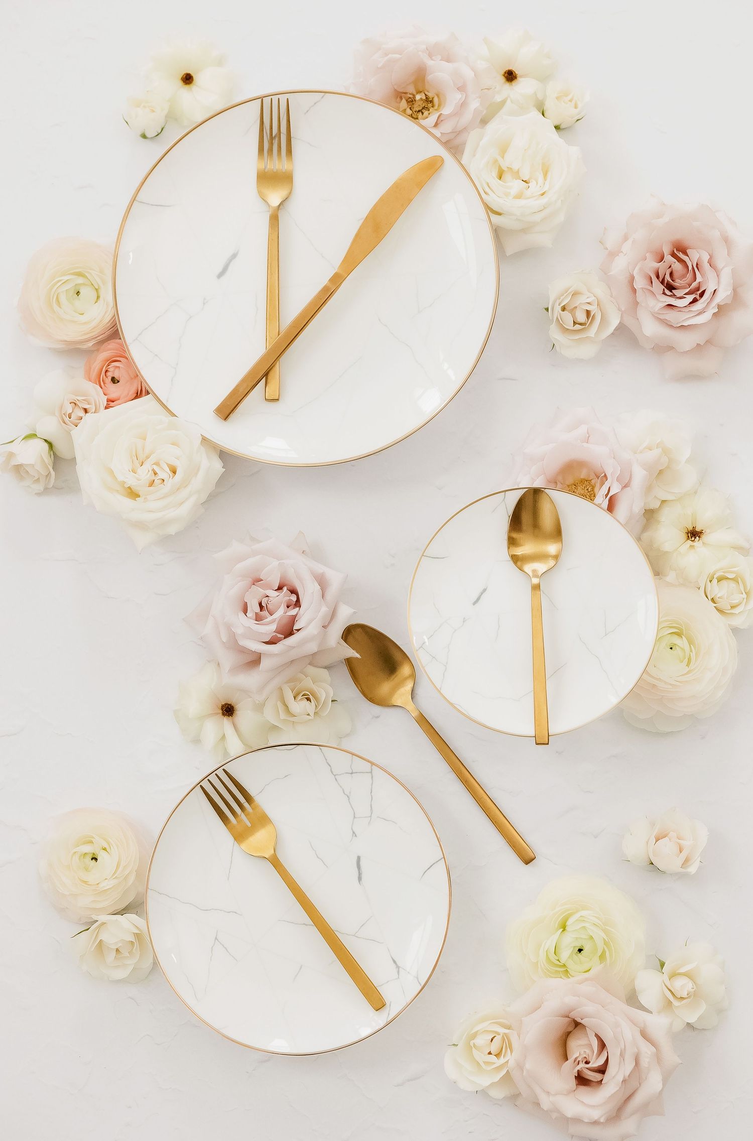 White marble plates with gold cutlery arranged among delicate pink and white roses.