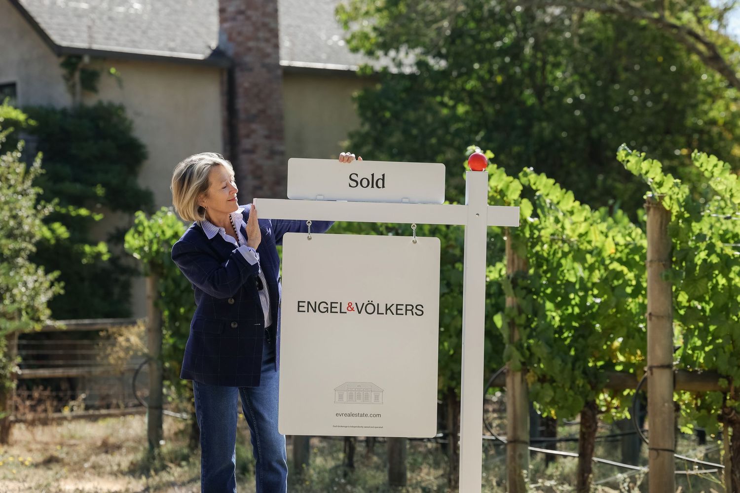 Real estate sold sign posted in front of green landscaping.