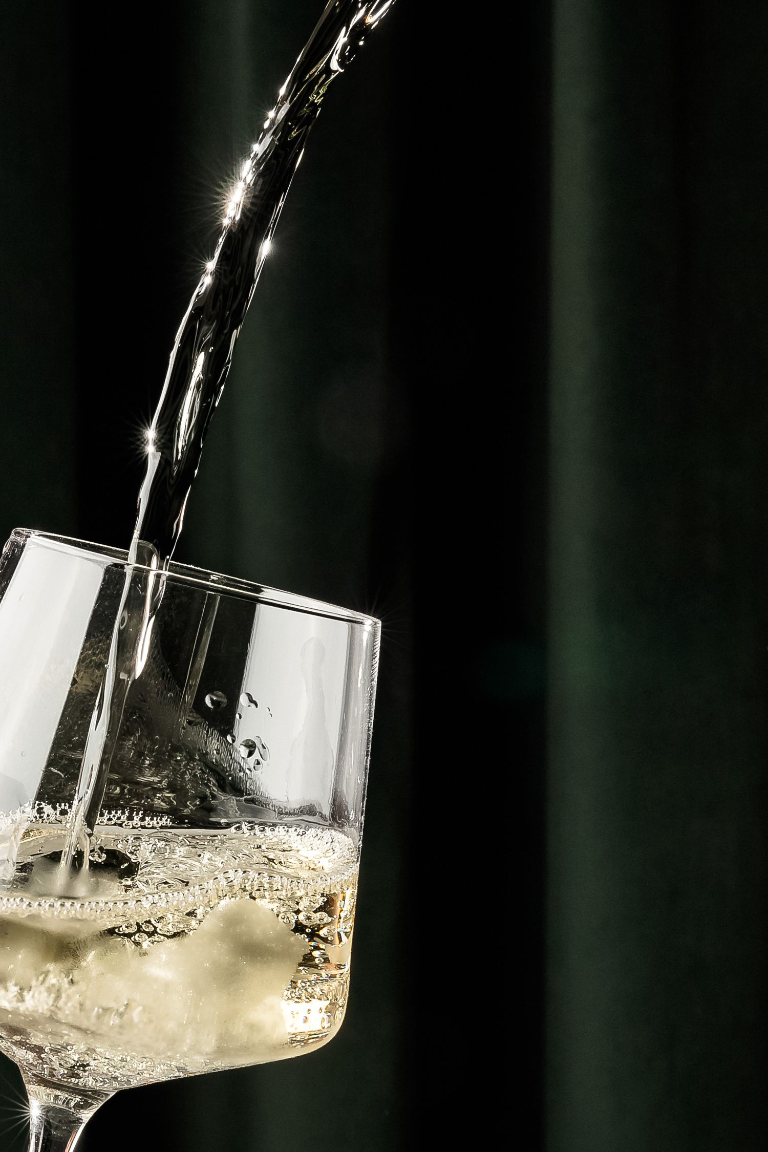 Clear sparkling liquid being poured into modern angular wine glass.