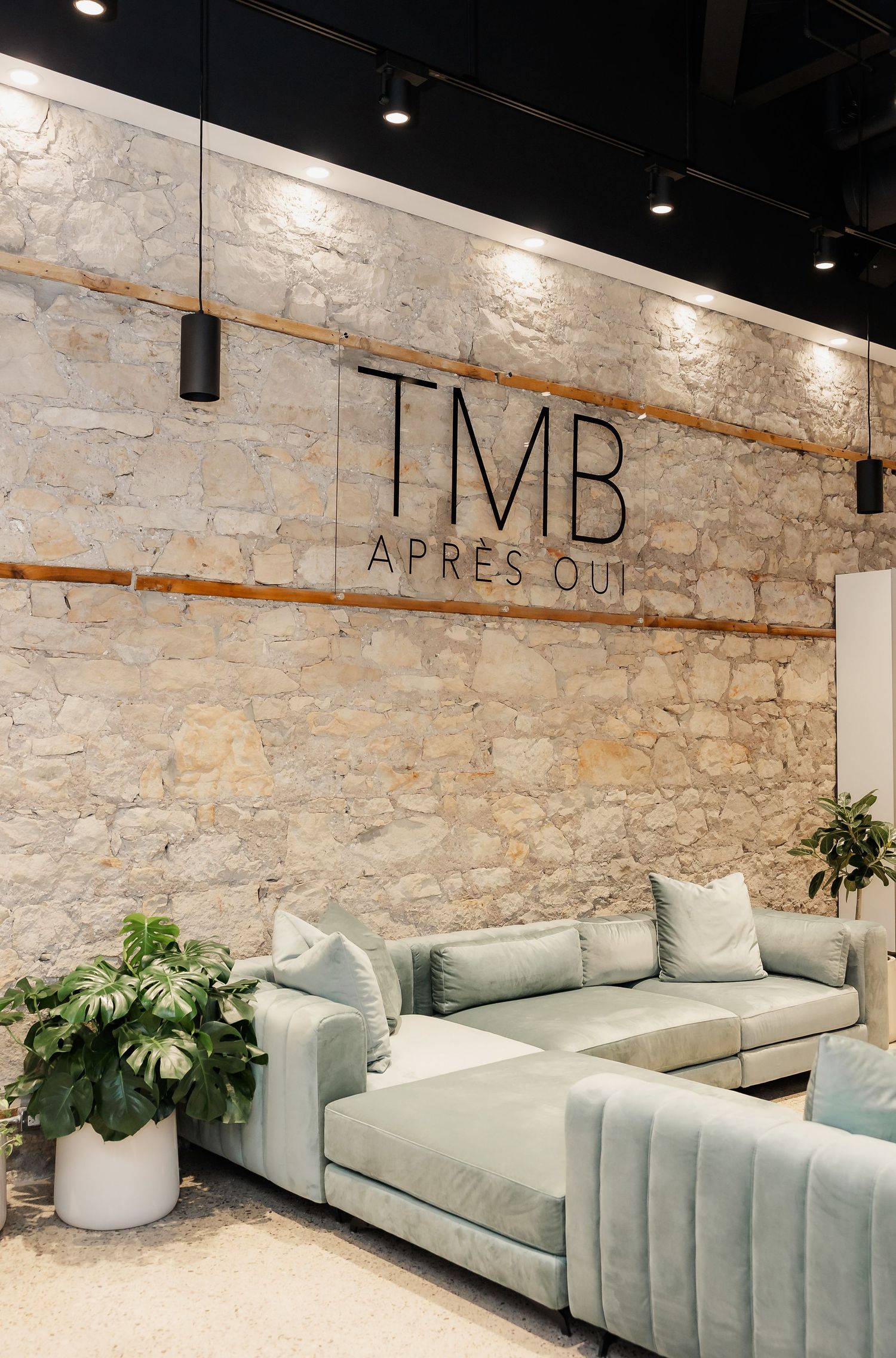 Modern lounge area with mint green velvet sofa against exposed stone wall with LMB signage.