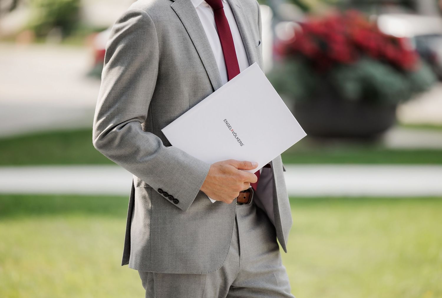 Professional in a gray suit holding paperwork while walking outside a modern building.