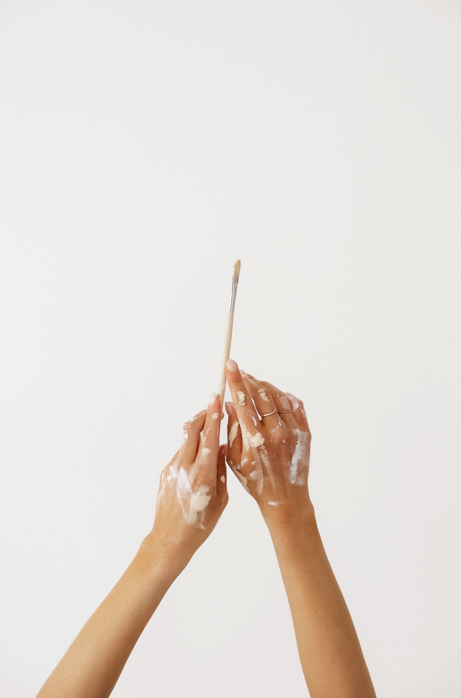 Hands holding up wooden paint brushes against a white background in sequence.