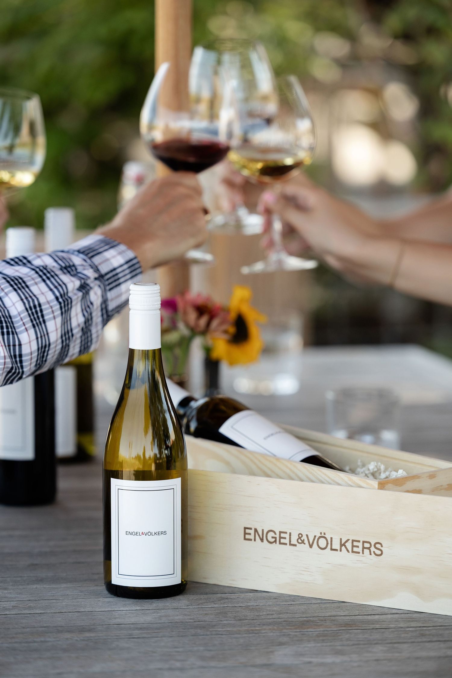 Wooden wine box with bottle and glasses arranged on outdoor table during wine tasting event.