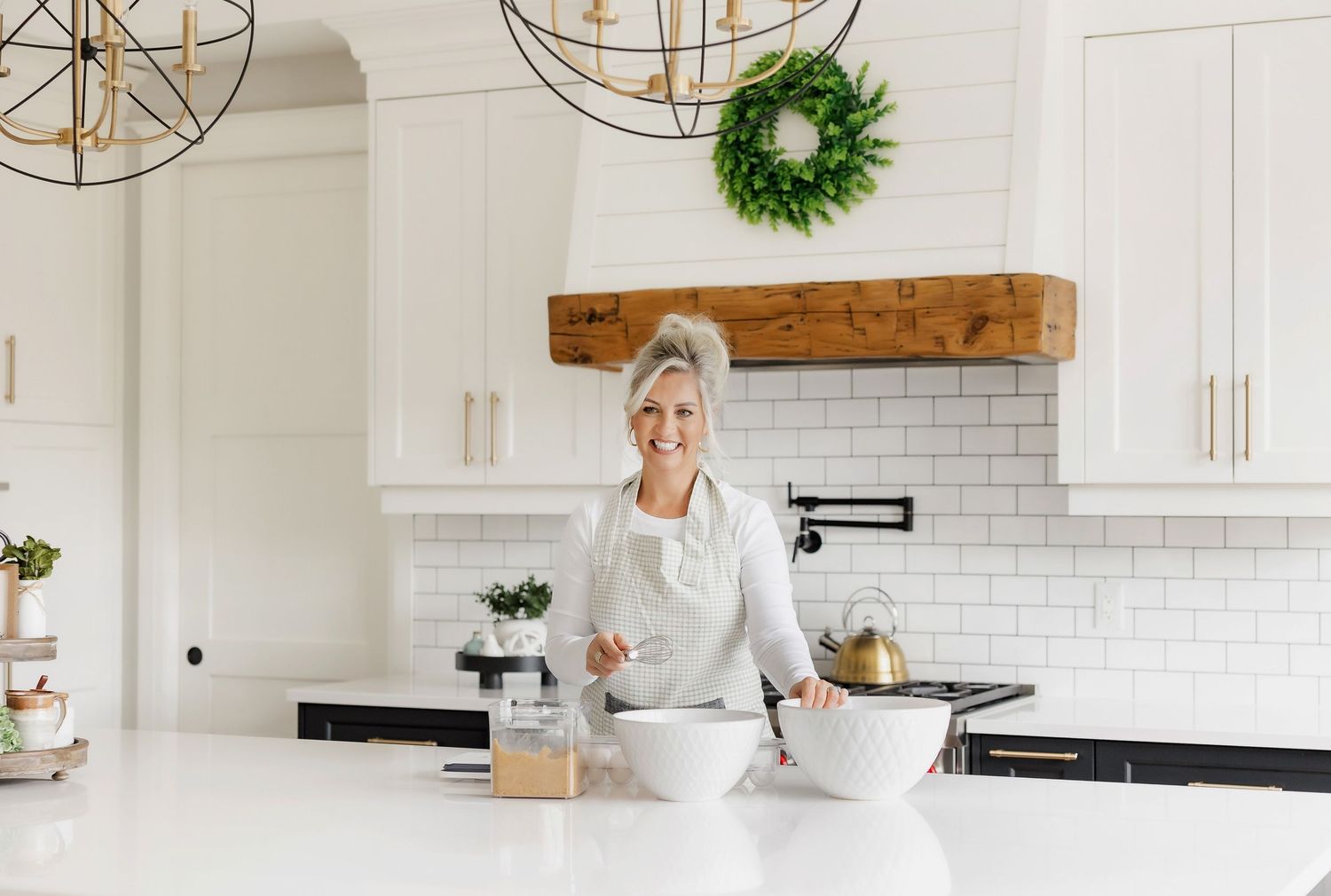Modern white kitchen with rustic wooden beam, subway tile backsplash, and decorative wreath accent.