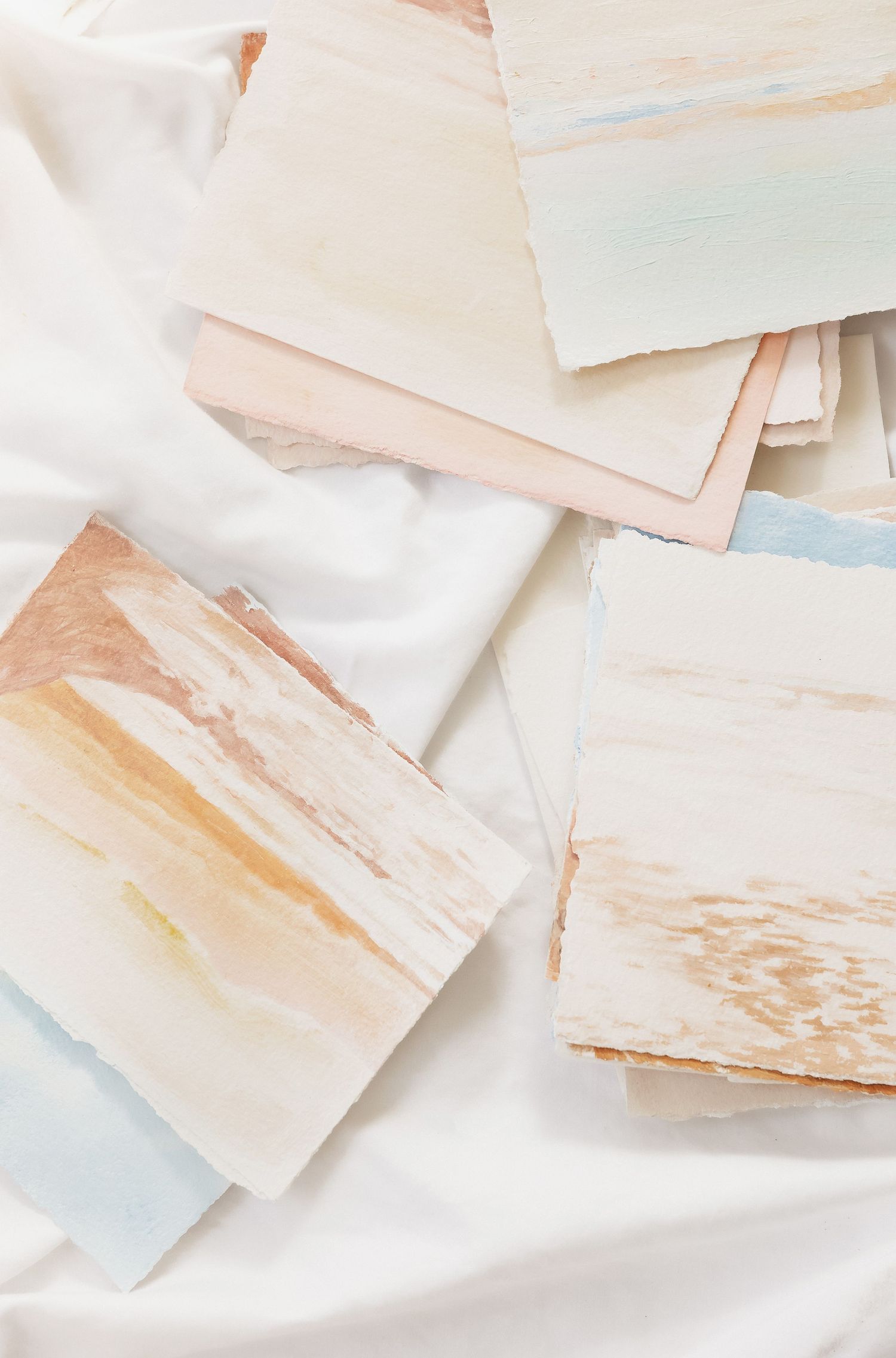 Soft pastel watercolor paper swatches arranged on white fabric with delicate peach and blue tones.