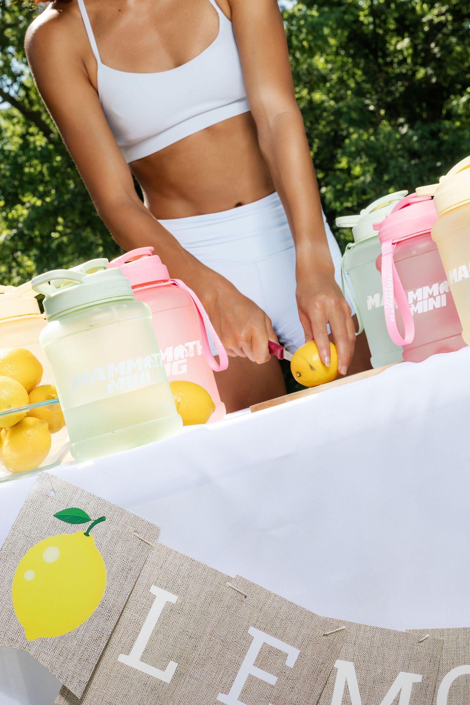 Close-up of white athletic wear and colorful drink containers with fresh lemons on lemonade stand.