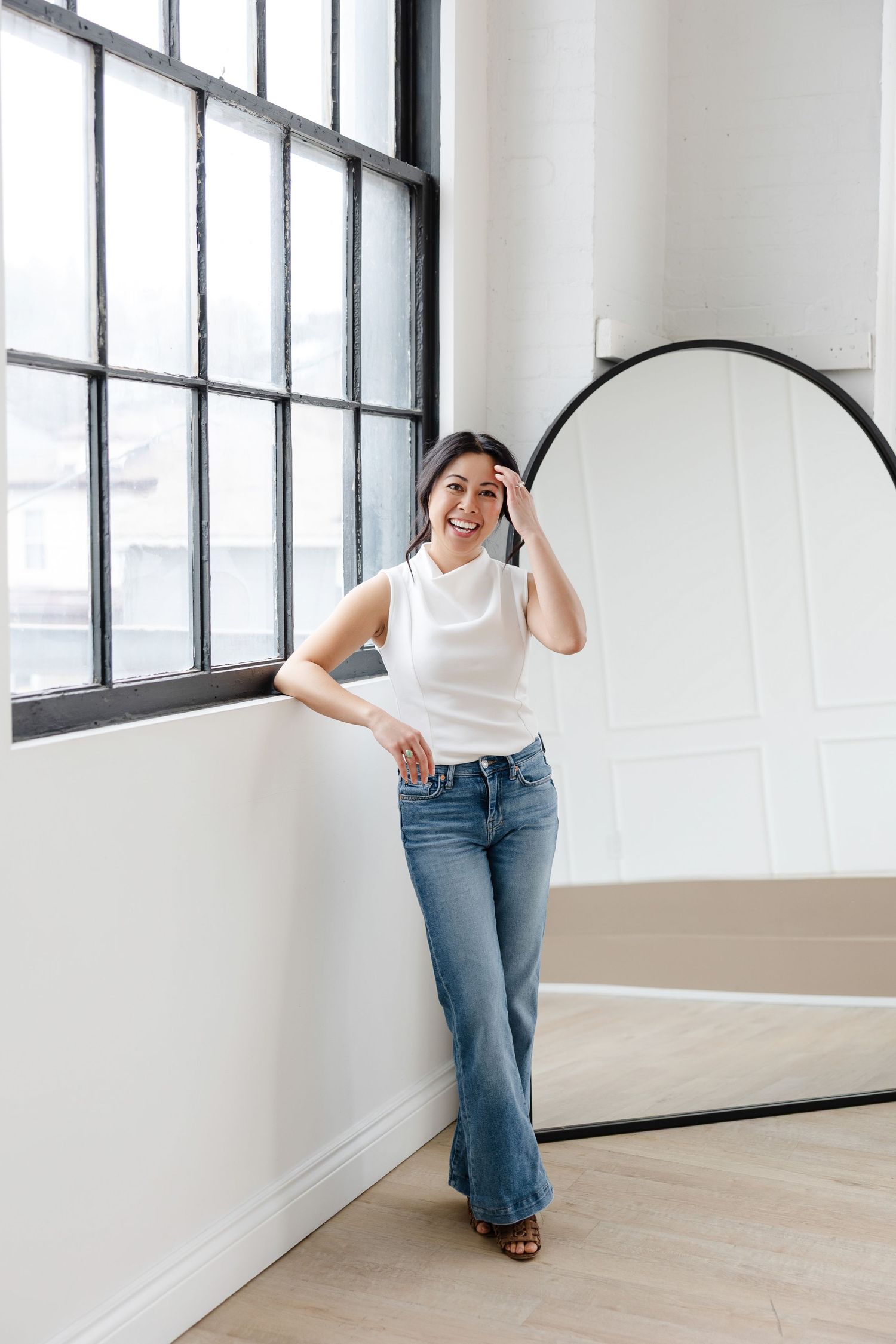 Playful studio portrait session with denim and white top against minimalist background.