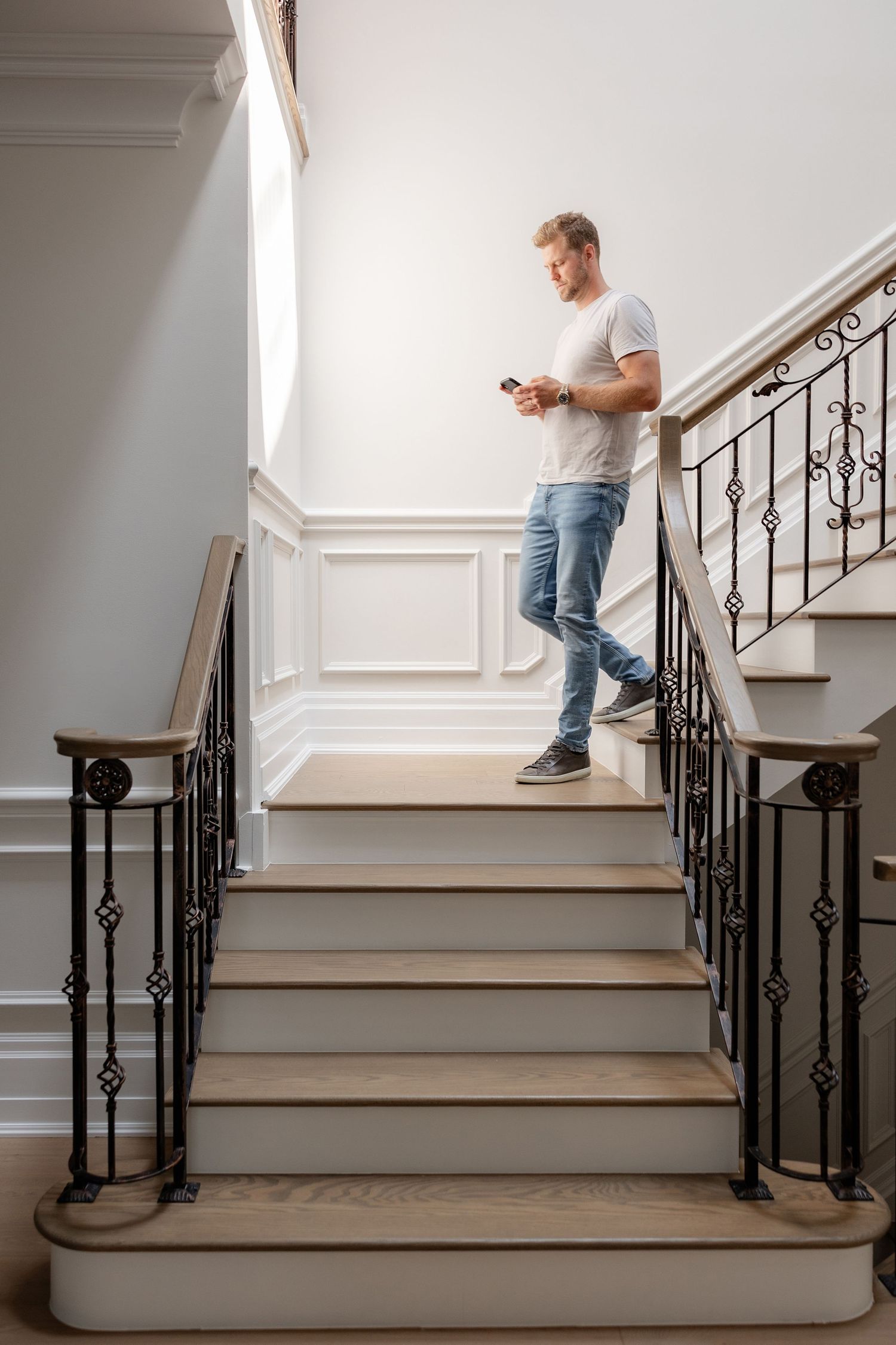 Person in casual attire walking up elegant white stairs with ornate black metal railings.