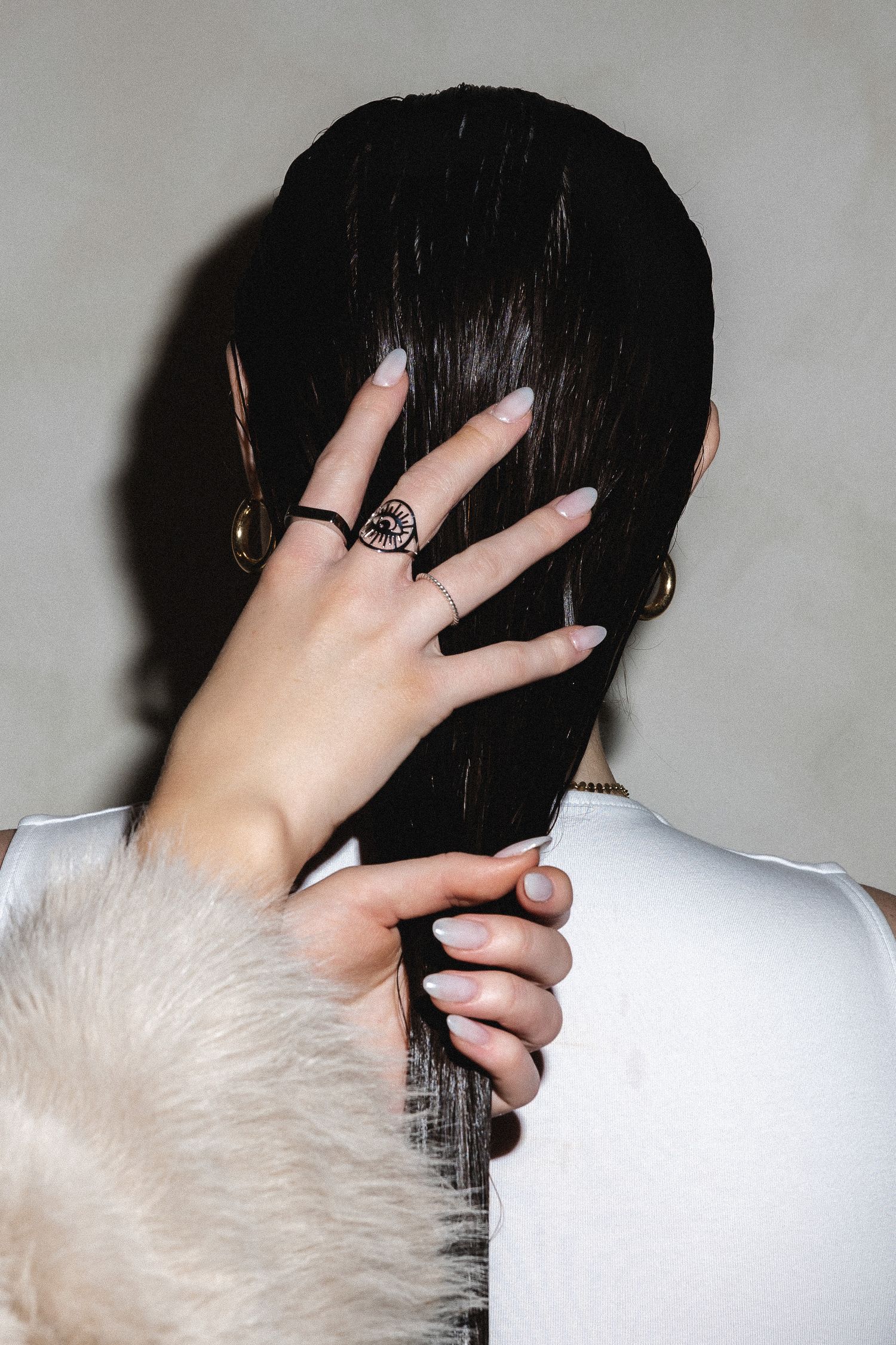Hands styling wet dark hair from behind against light background.
