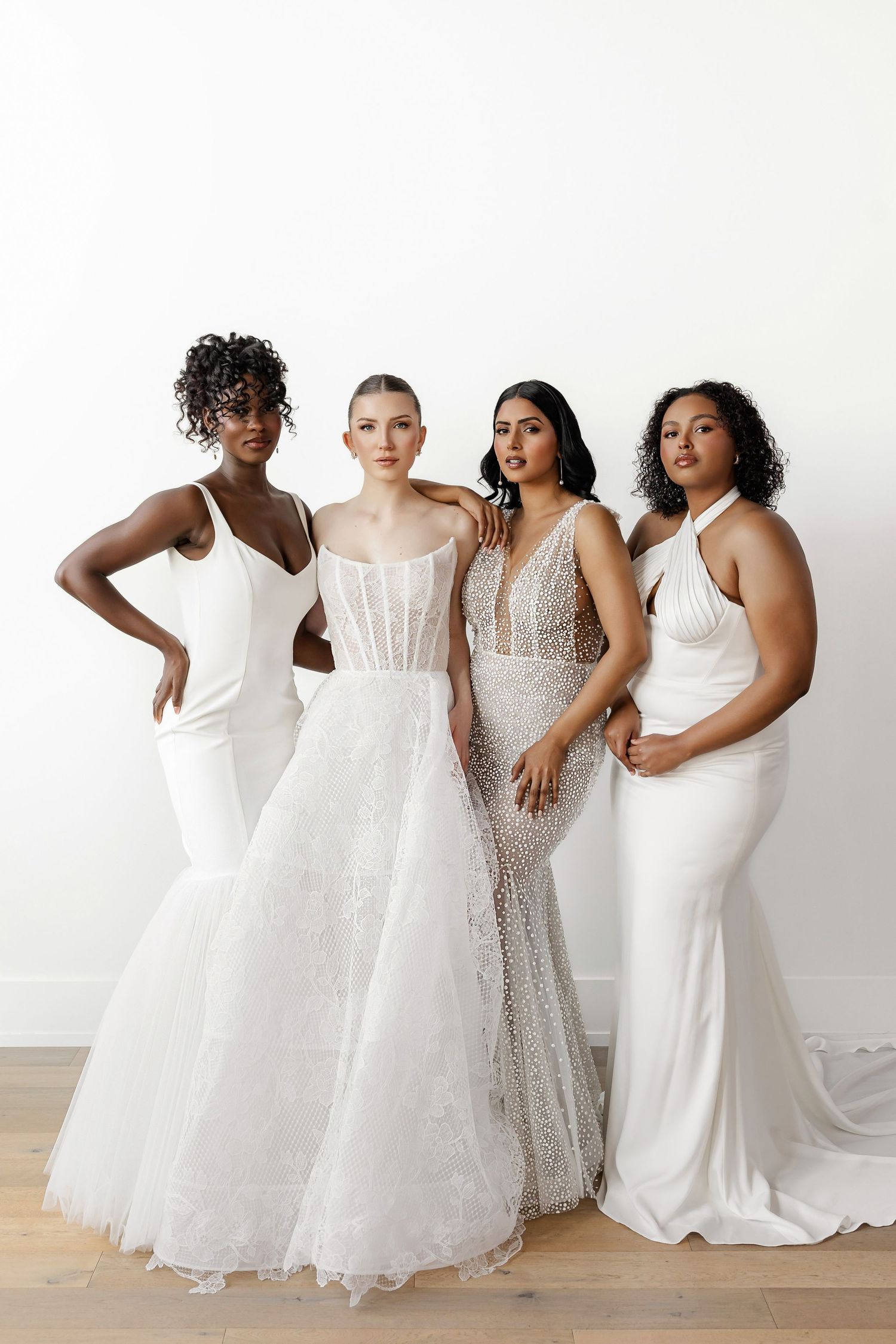 Models wearing diverse styles of white wedding gowns posed together in a studio setting.