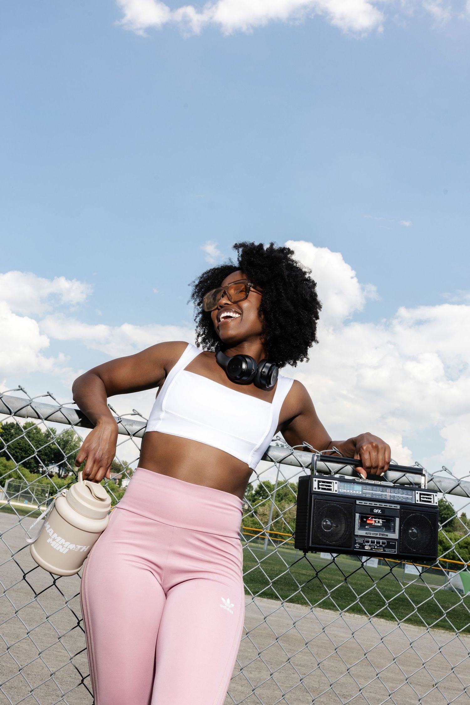 Person in pink workout attire relaxing on grass with a retro boombox on a sunny day.