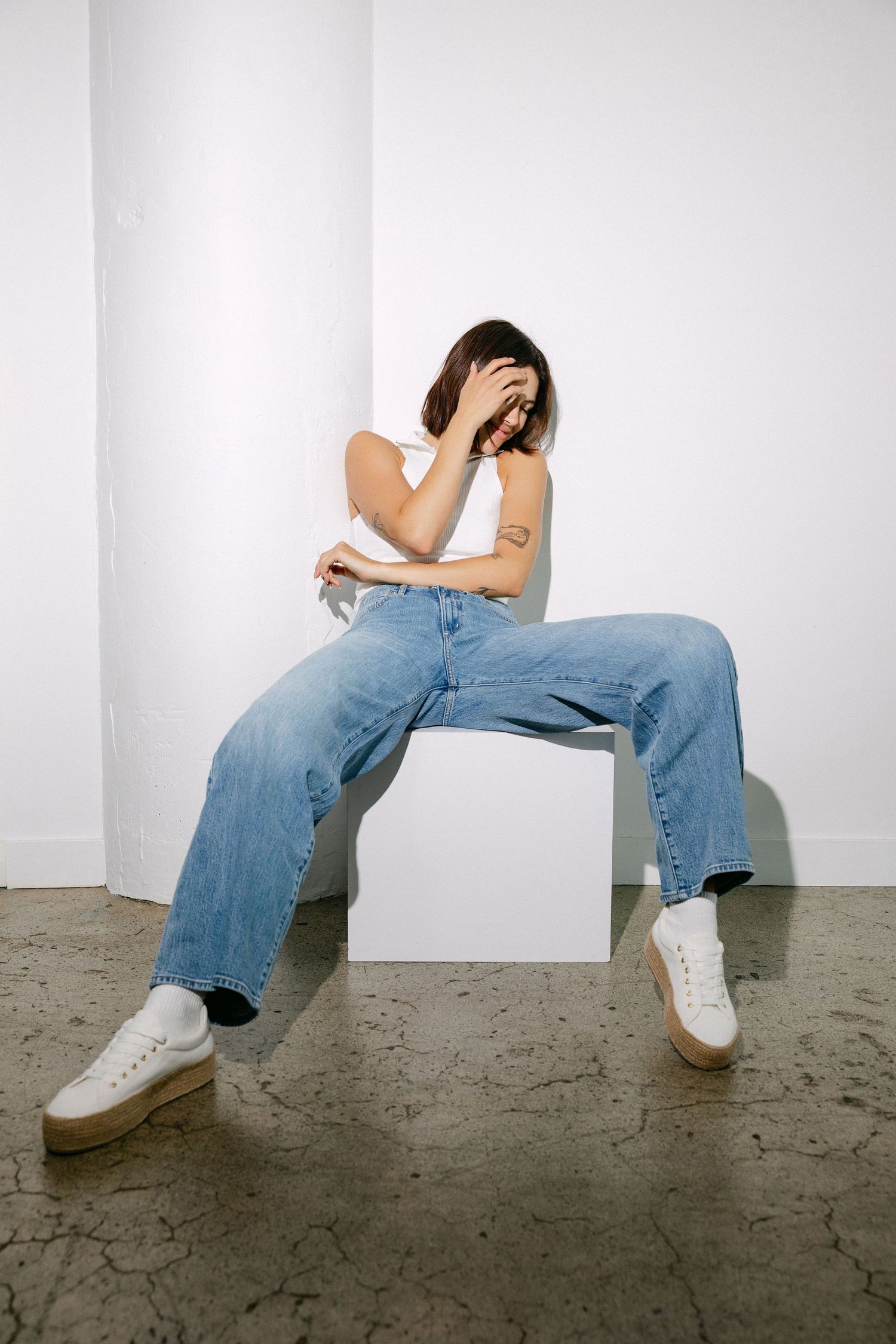 Artistic photo sequence showing relaxed poses on white cube with baggy jeans and white sneakers.