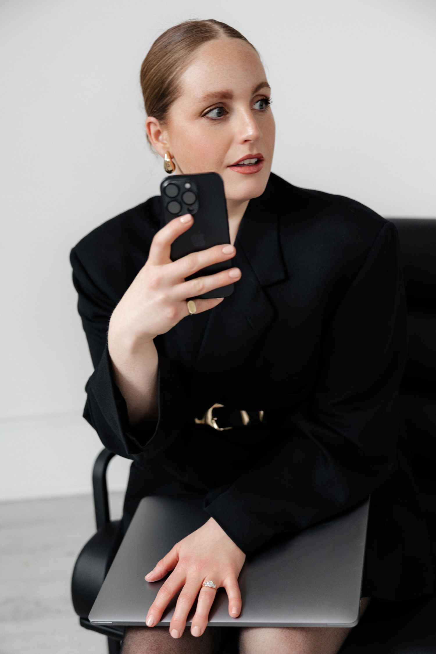Elegant portrait showing person with iPhone and MacBook in black business attire.