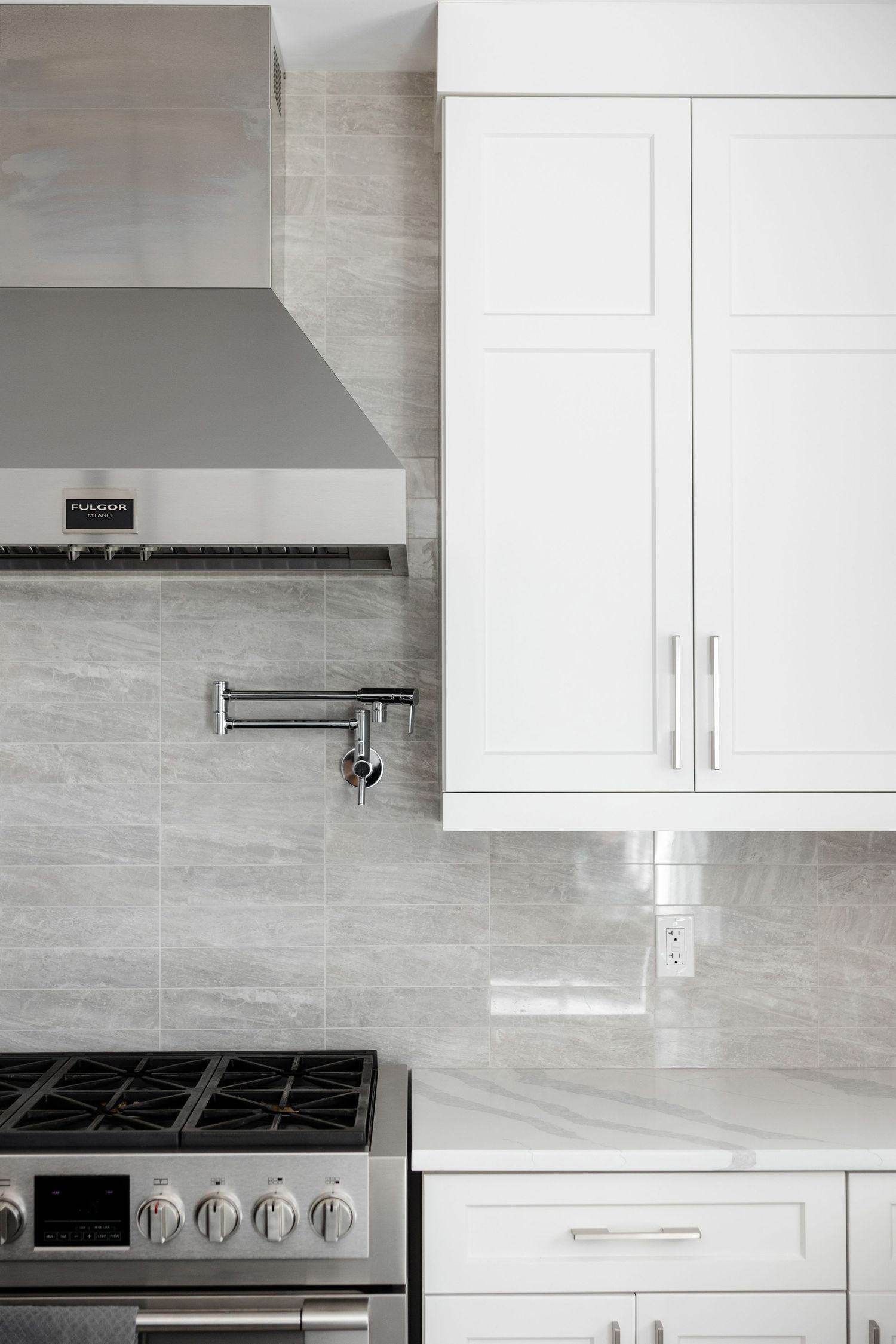 Modern white kitchen with stainless steel appliances and light gray backsplash.