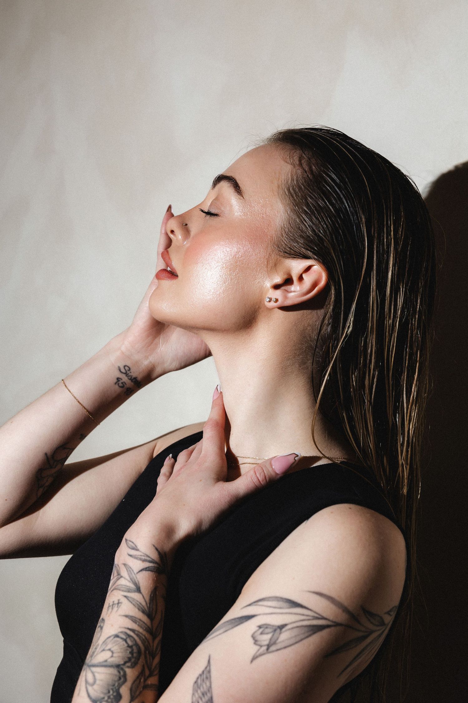 Artistic profile shot showing wet hair and tattoos against light background.