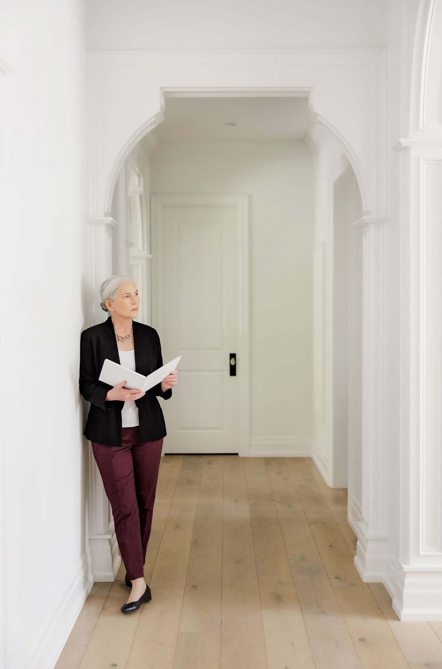 Business person reviews paperwork while standing in elegant white hallway with arched doorway.