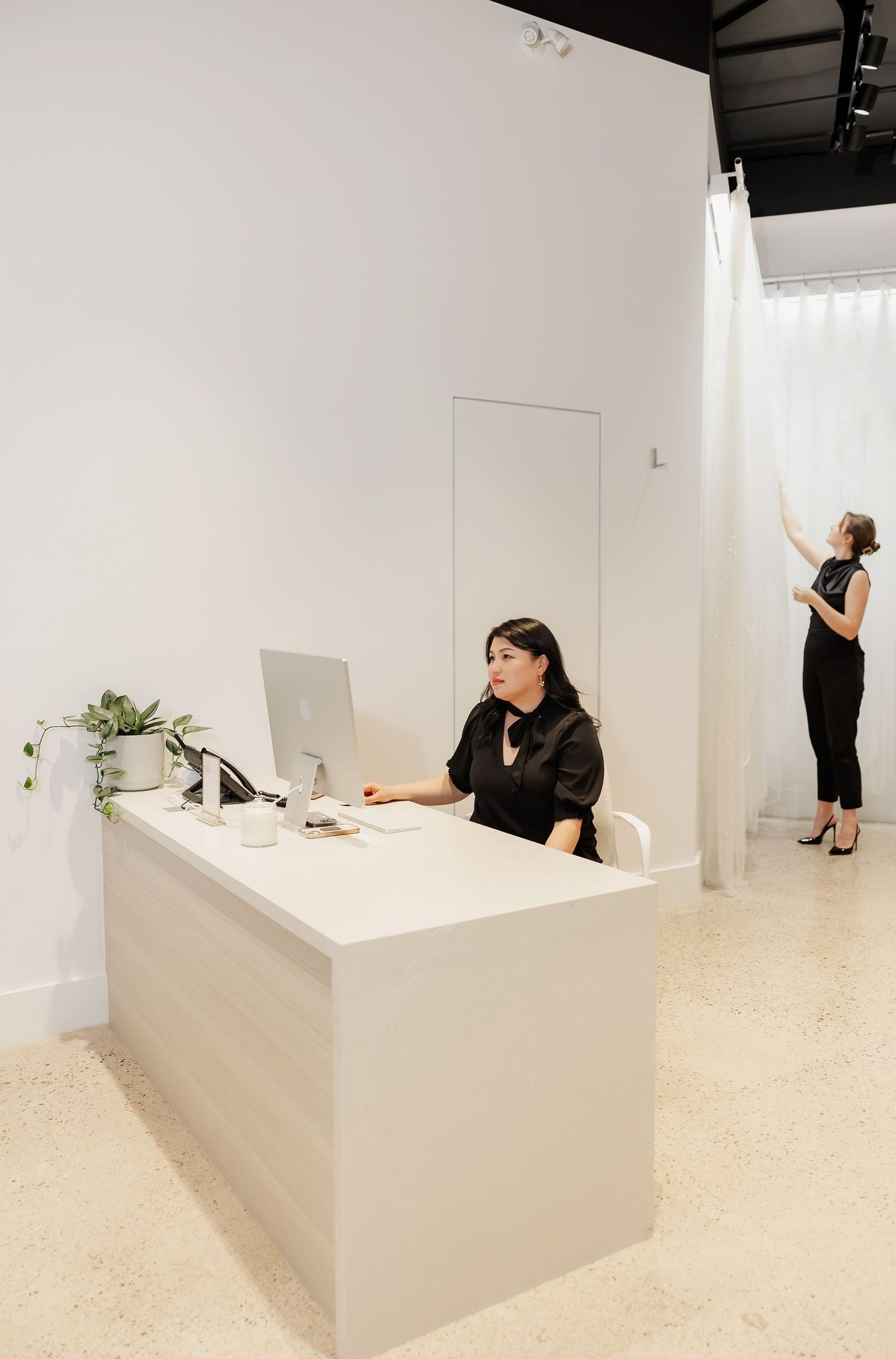 People interact playfully at a modern white retail counter in a minimalist store setting.