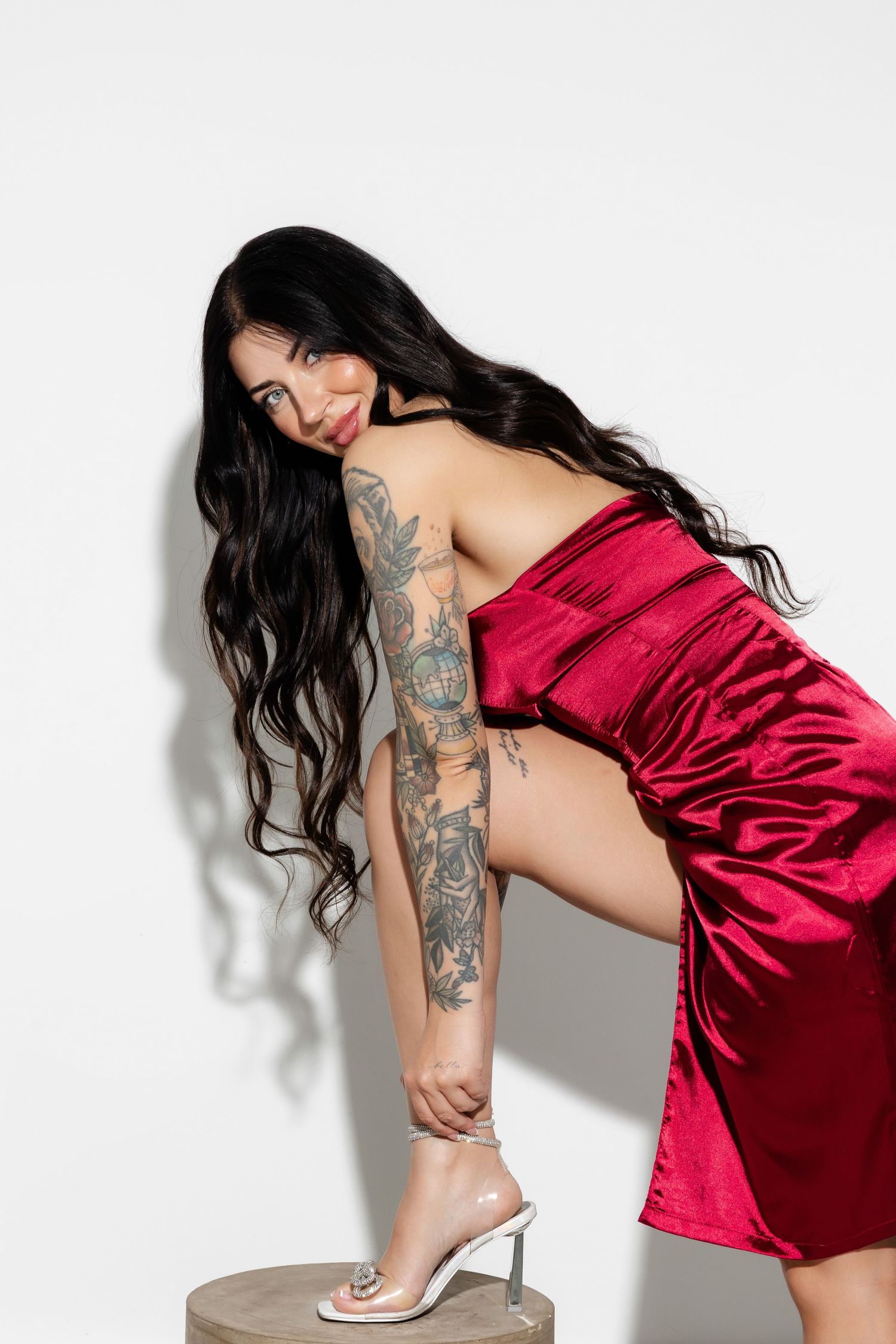 Model in red satin dress posing against white background.