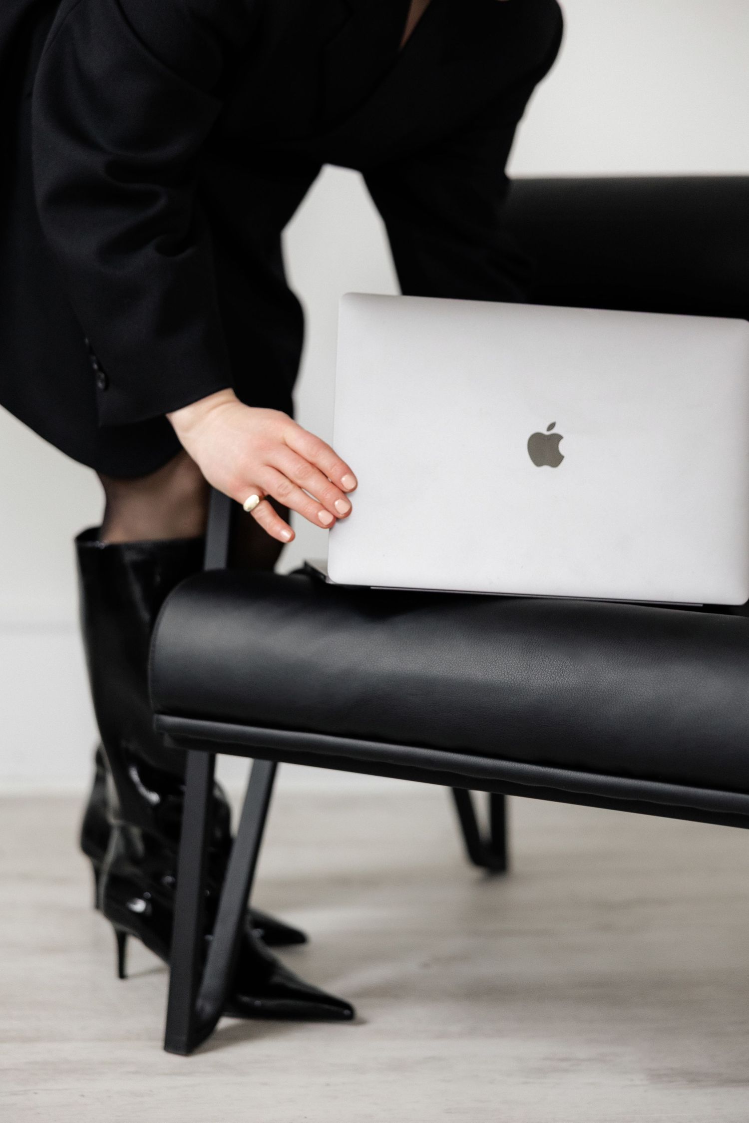 Hand reaching for MacBook laptop on black leather chair showing minimalist workspace setup.