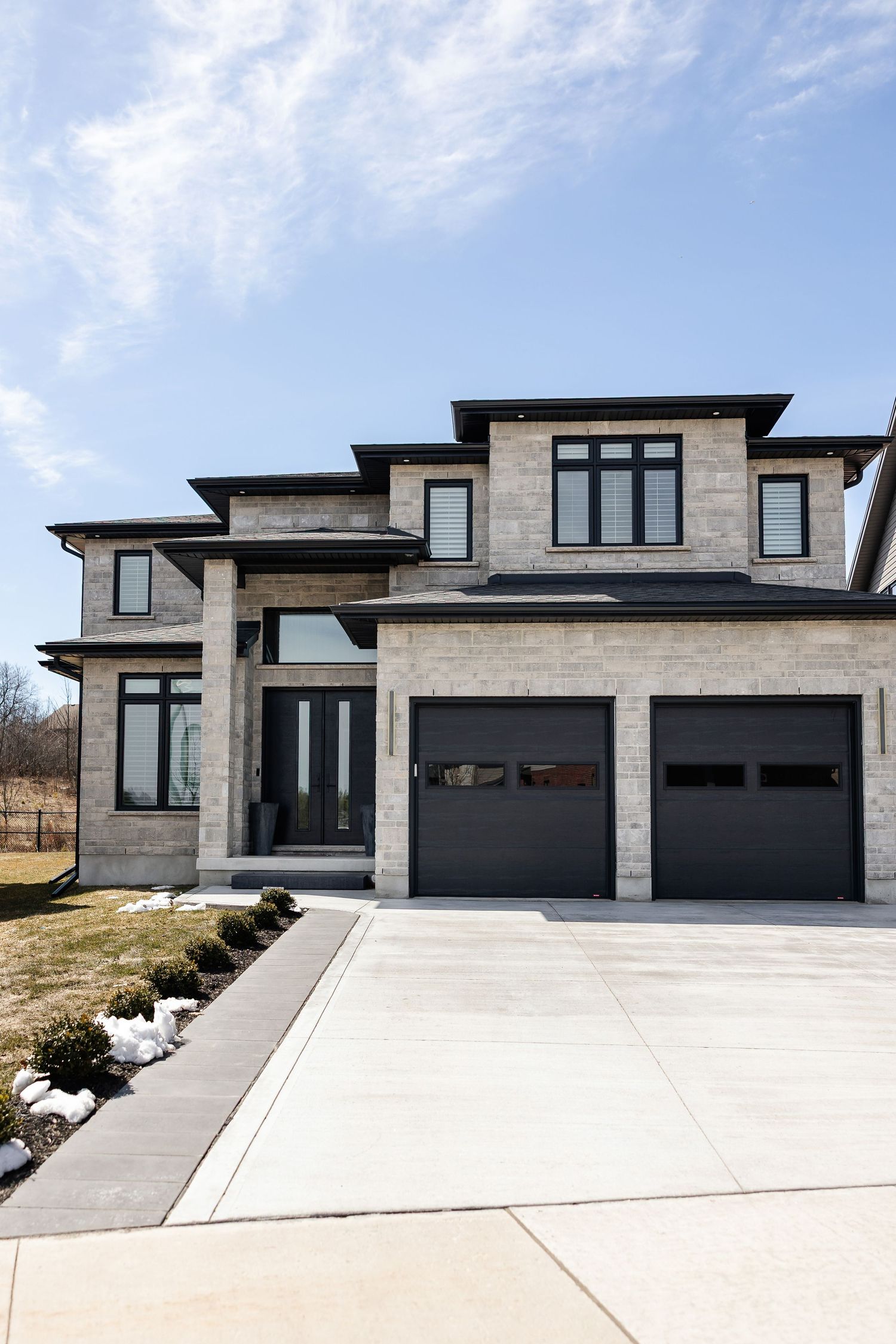 Contemporary gray stone house exterior with black trim and large driveway.