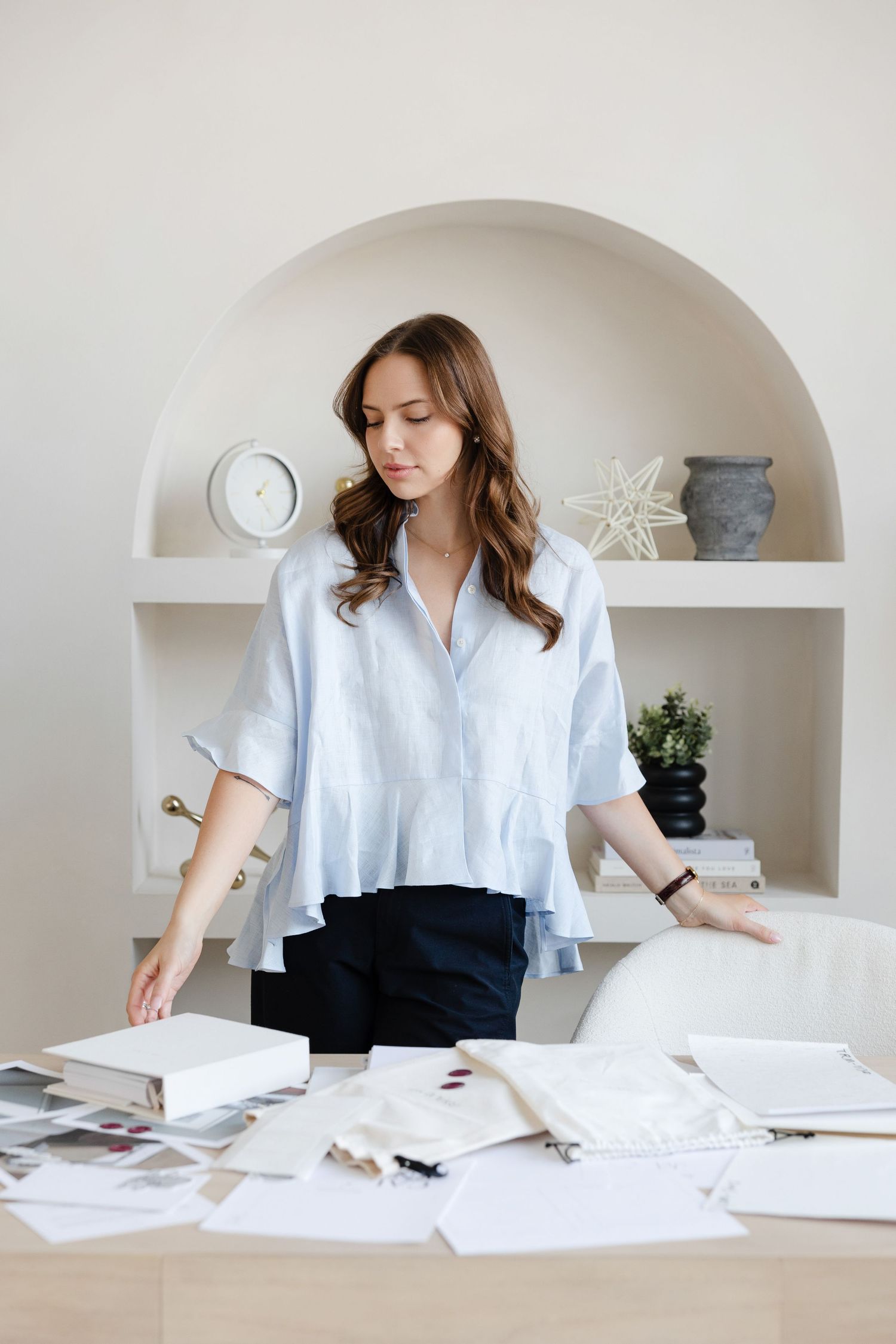 Designer reviewing documents at workspace with arched shelving displaying minimal decor.