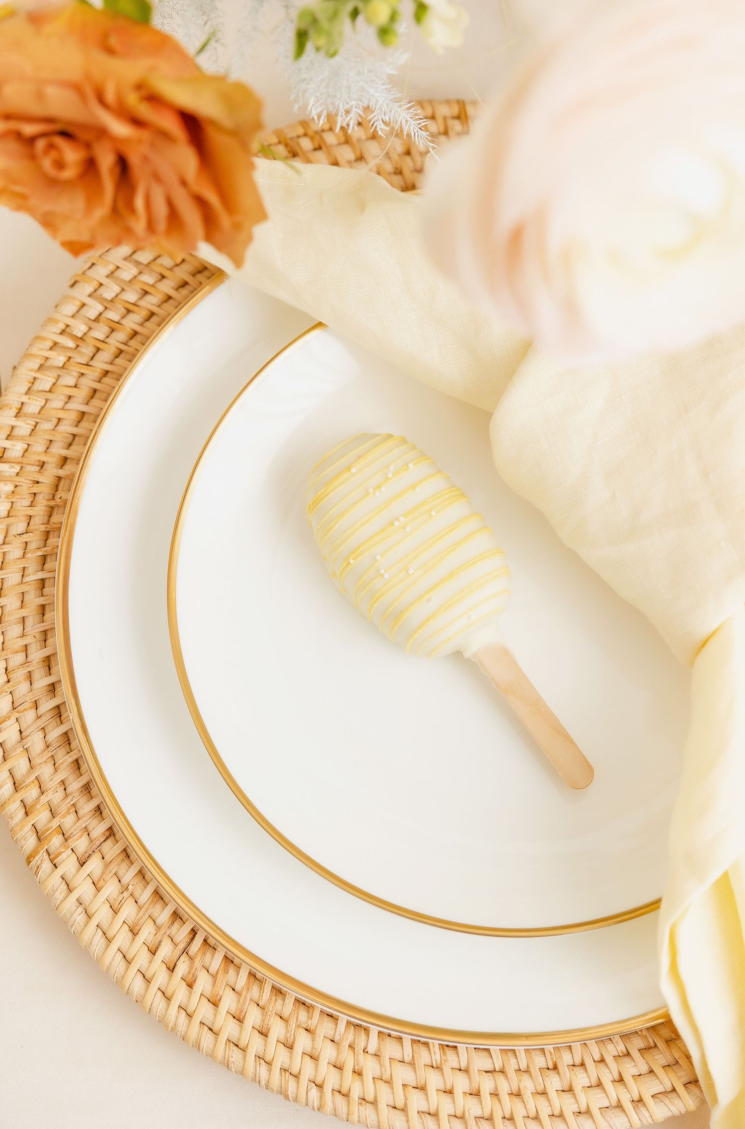 Close-up of white plates with gold trim on woven charger with cream napkin.