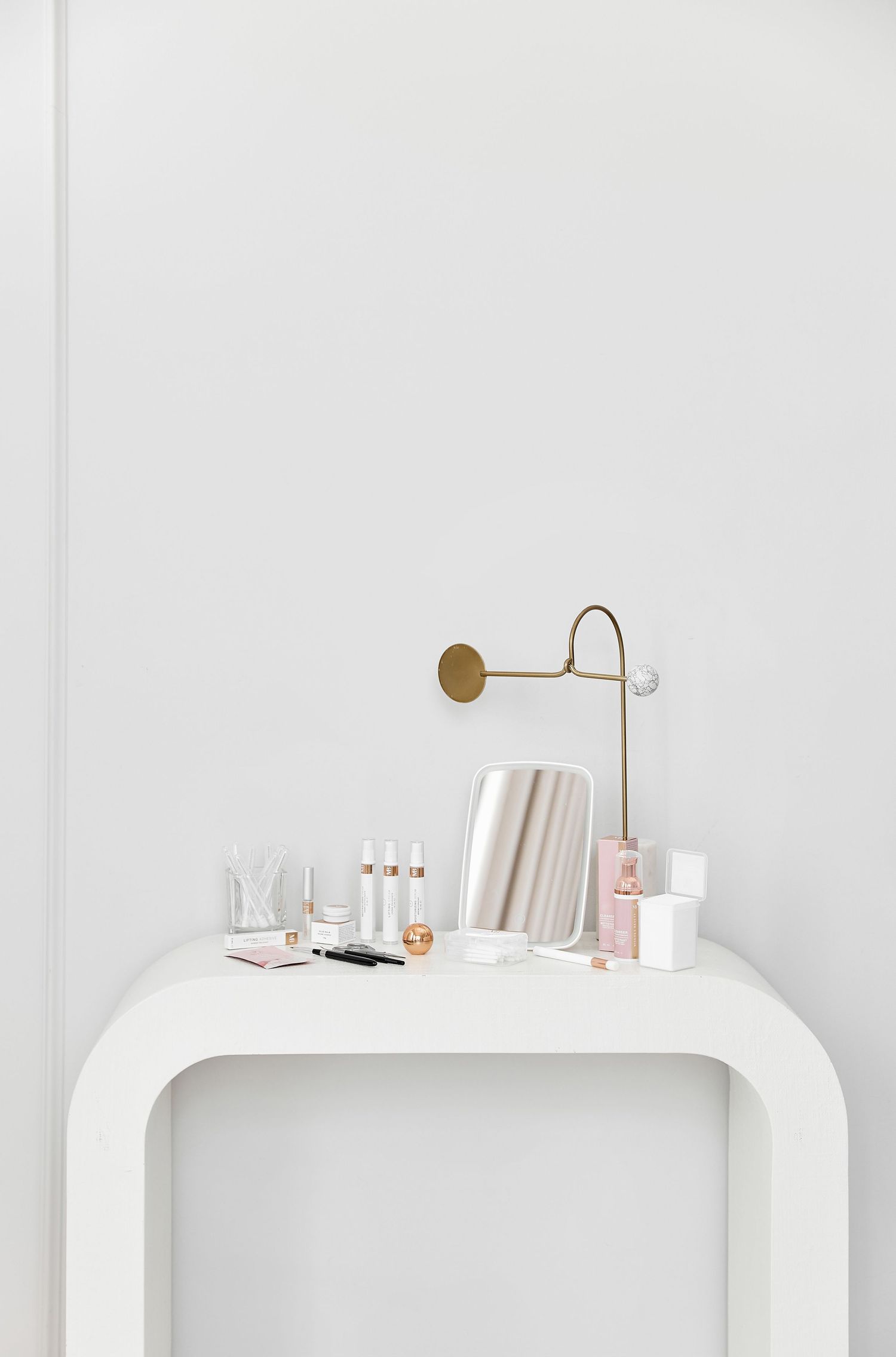 Minimalist white shelving display with gold accent lighting and beauty products.