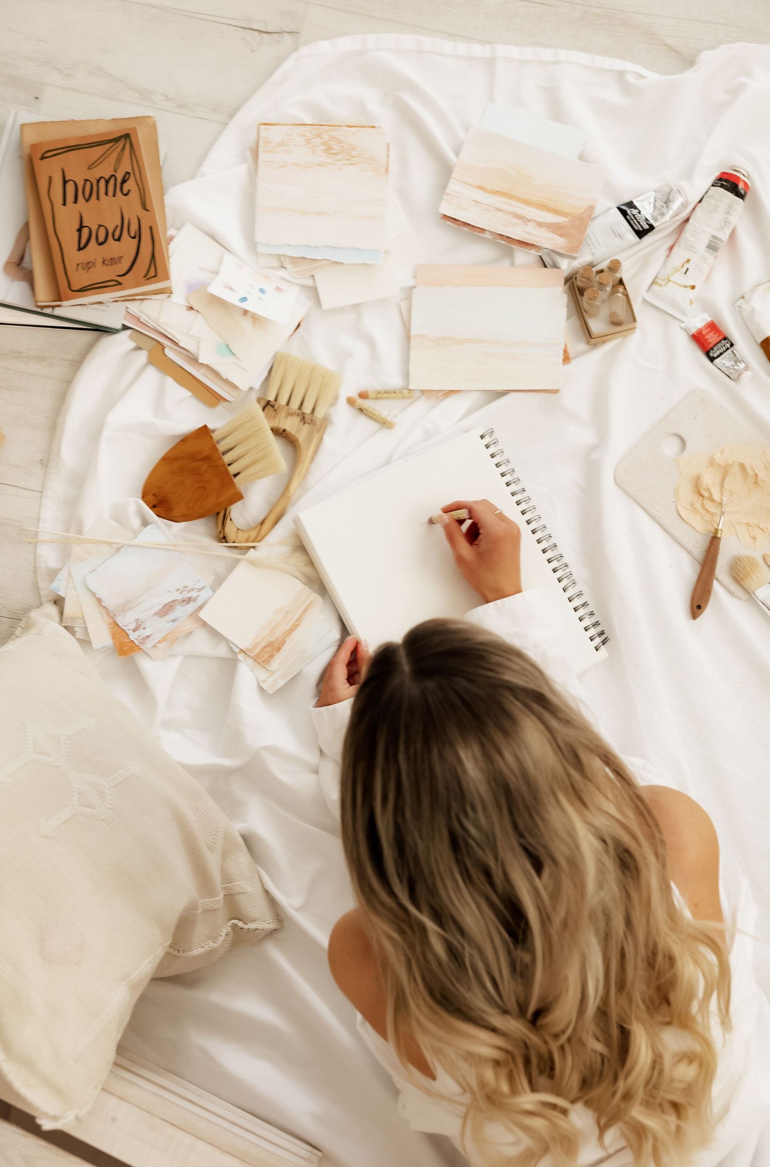 Artistic flatlay with notebooks, brushes and wooden accessories on white background.