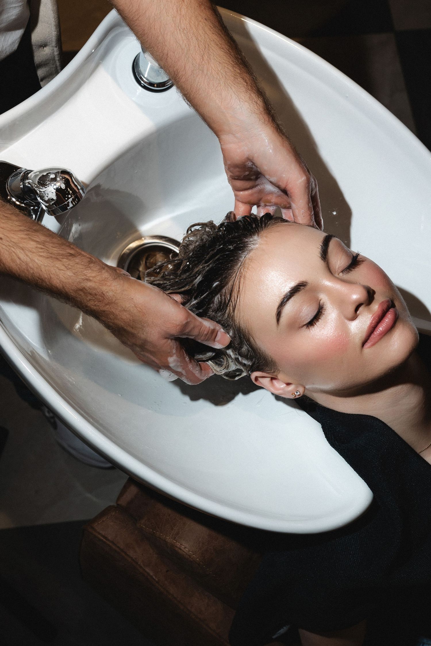 Hair being washed in a salon sink with dark hair laid back against white porcelain.