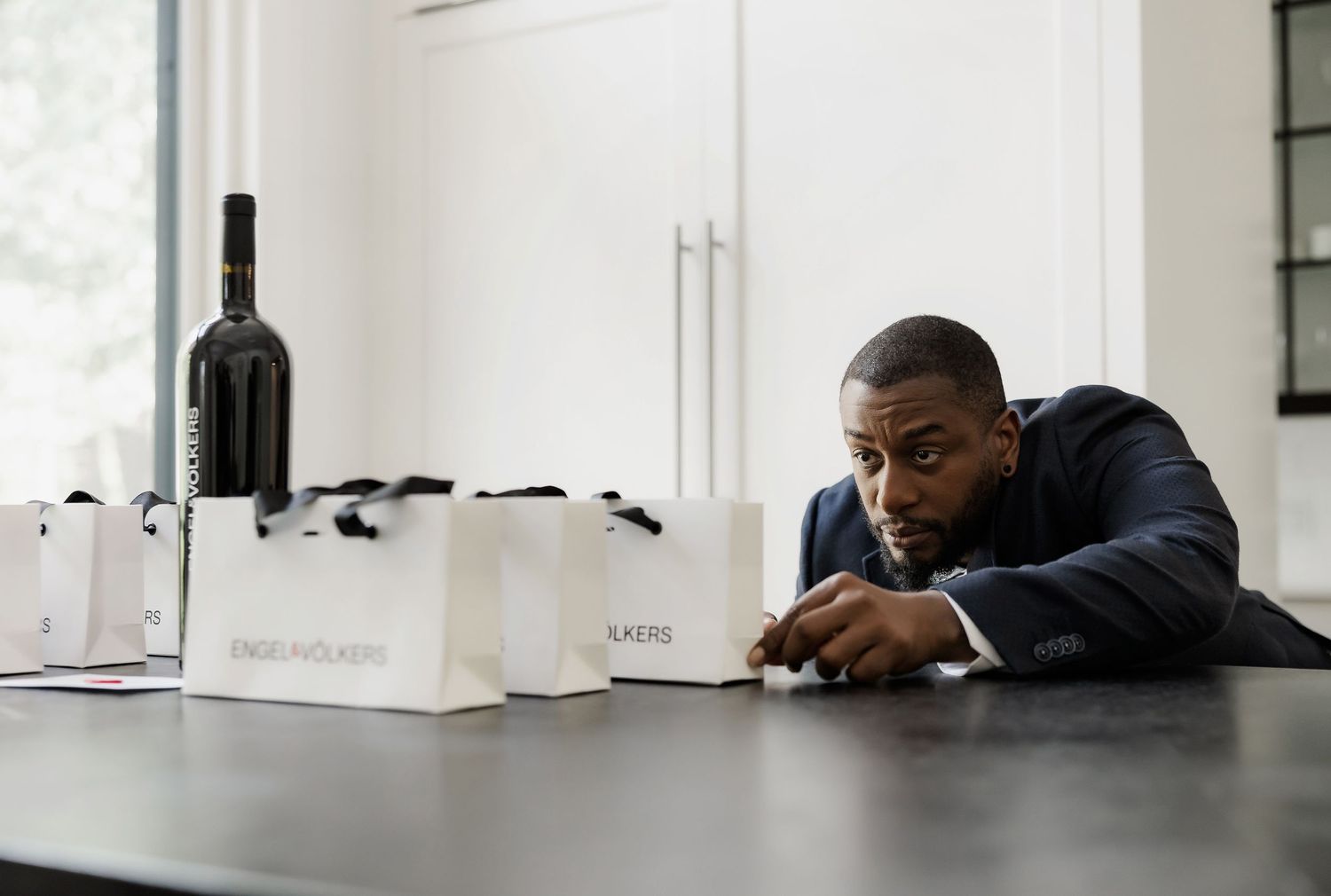 Business professional examines wine bottles and documents on dark table in formal setting.