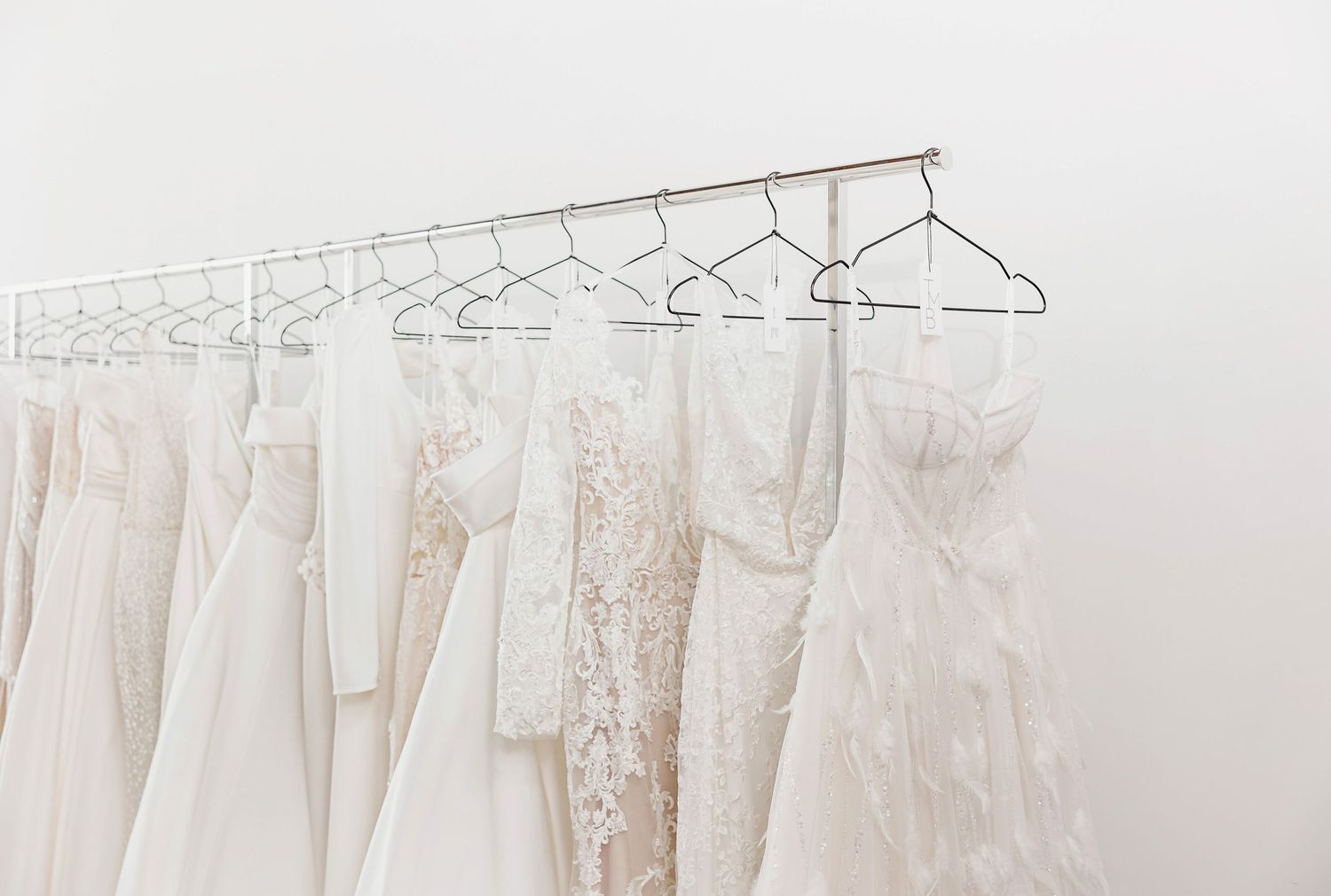 Wedding dresses hanging on display racks in a bridal boutique with natural lighting.