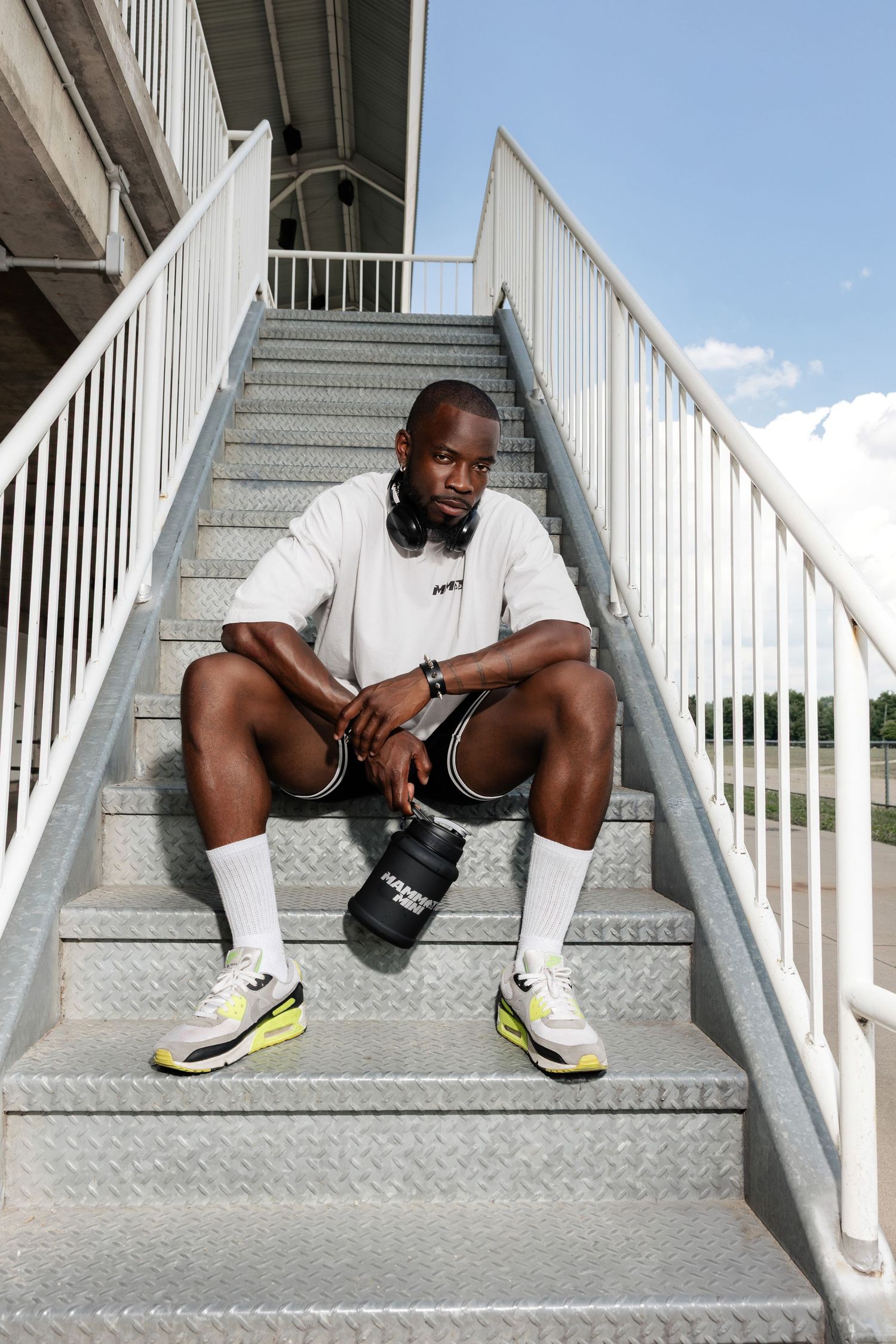 Person in white shirt and shorts sitting on concrete stairs with yellow sneakers.