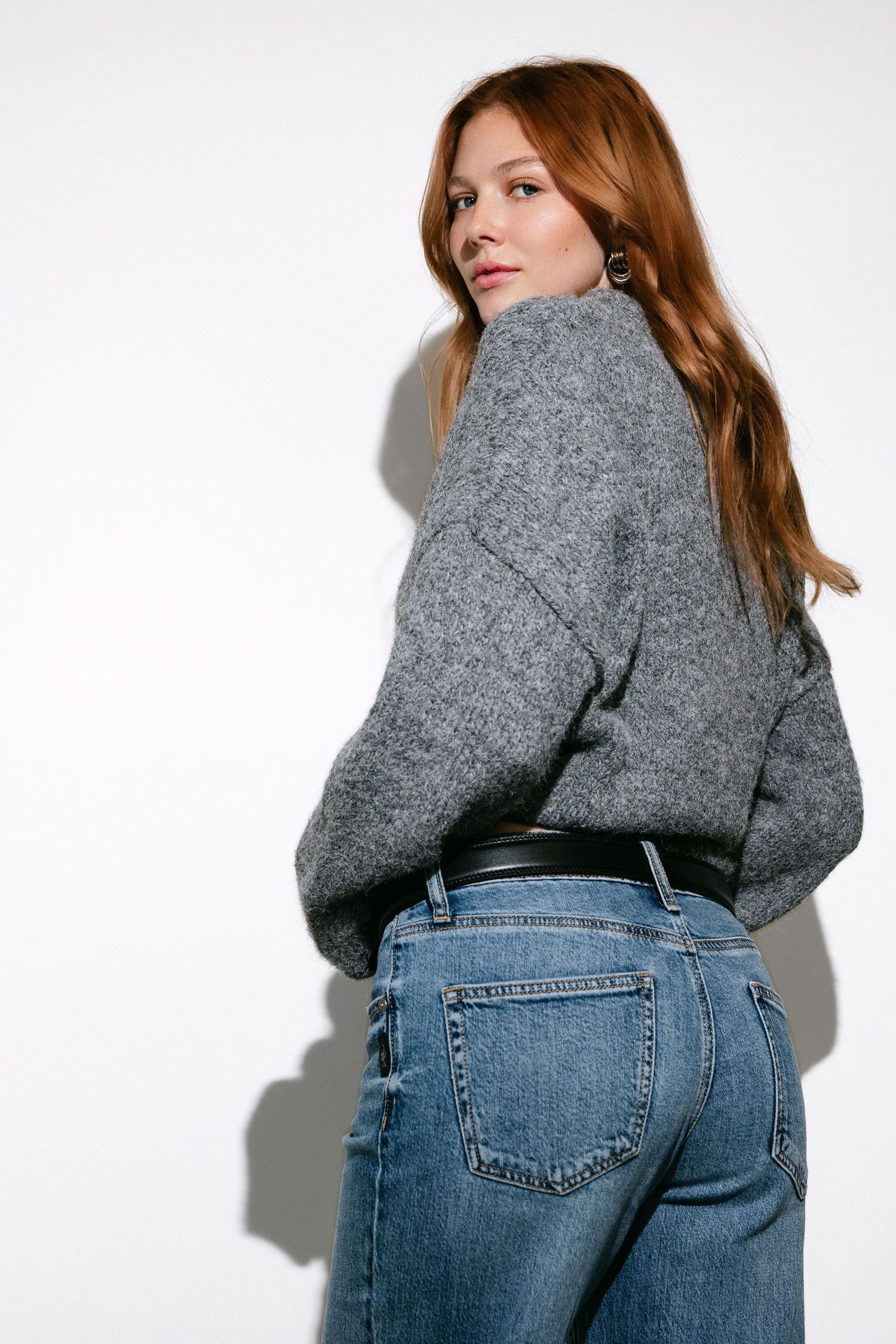 Side angle view of casual outfit featuring grey sweater and blue jeans.
