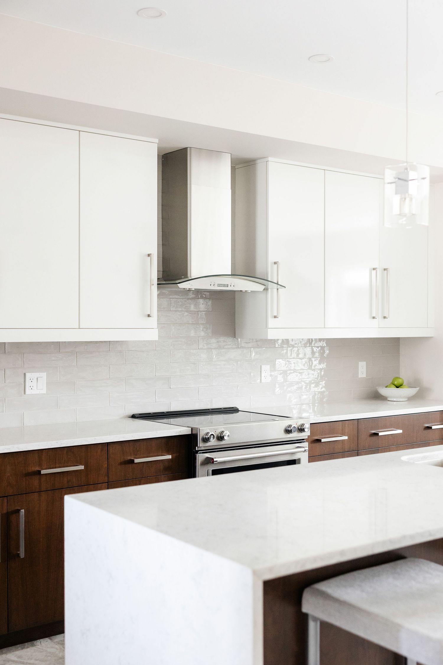 Luxury kitchen featuring white cabinets, dark wood accents, and quartz waterfall countertop.