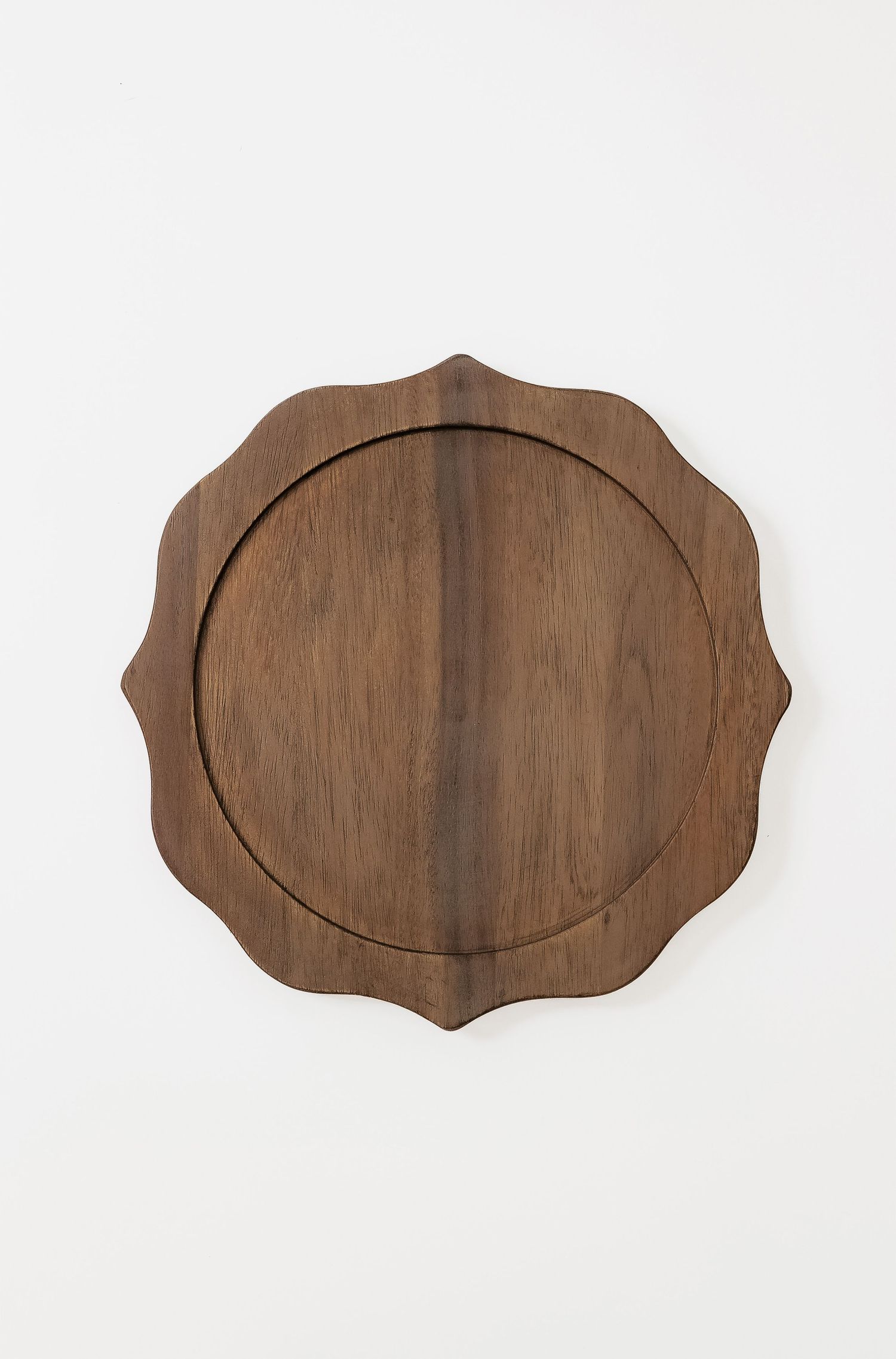 Scalloped edge wooden charger plate with circular detail in dark walnut finish.