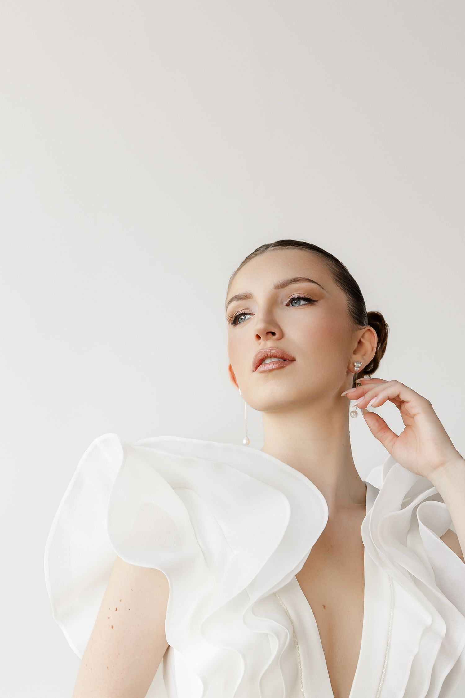 Artistic bridal portrait highlighting sculptural ruffled neckline detail against white background.