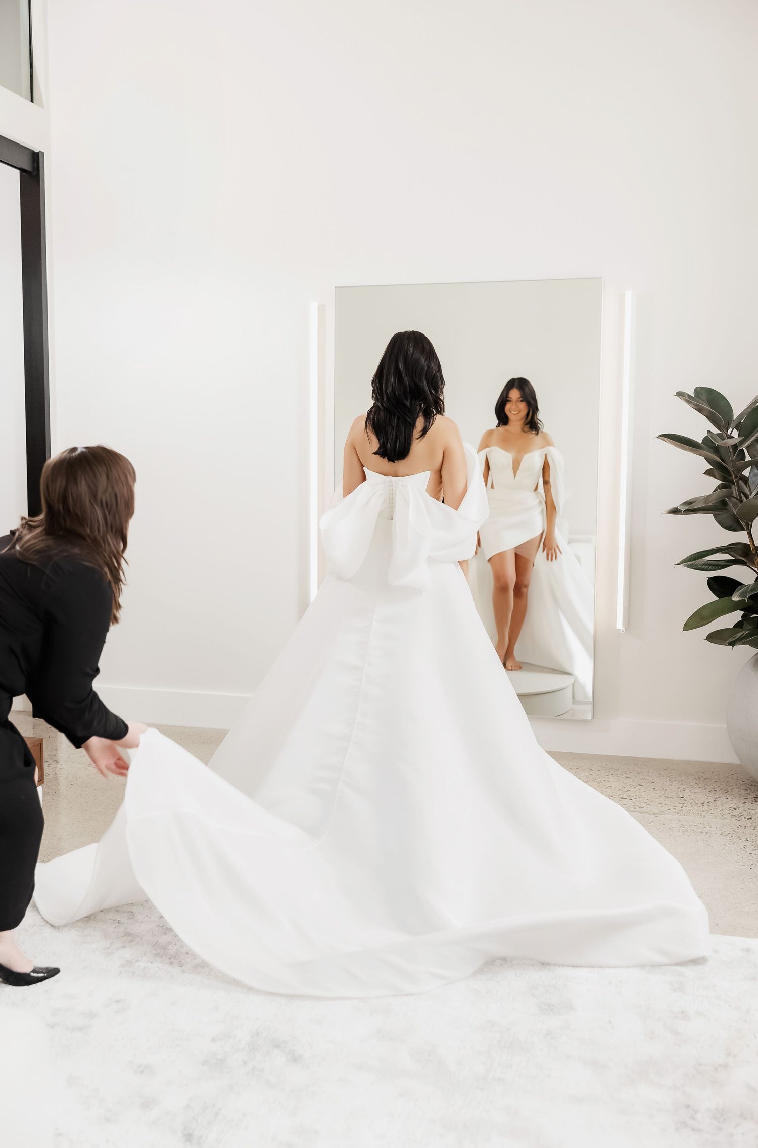 Bridal consultants assisting with long white wedding gown train in modern studio.