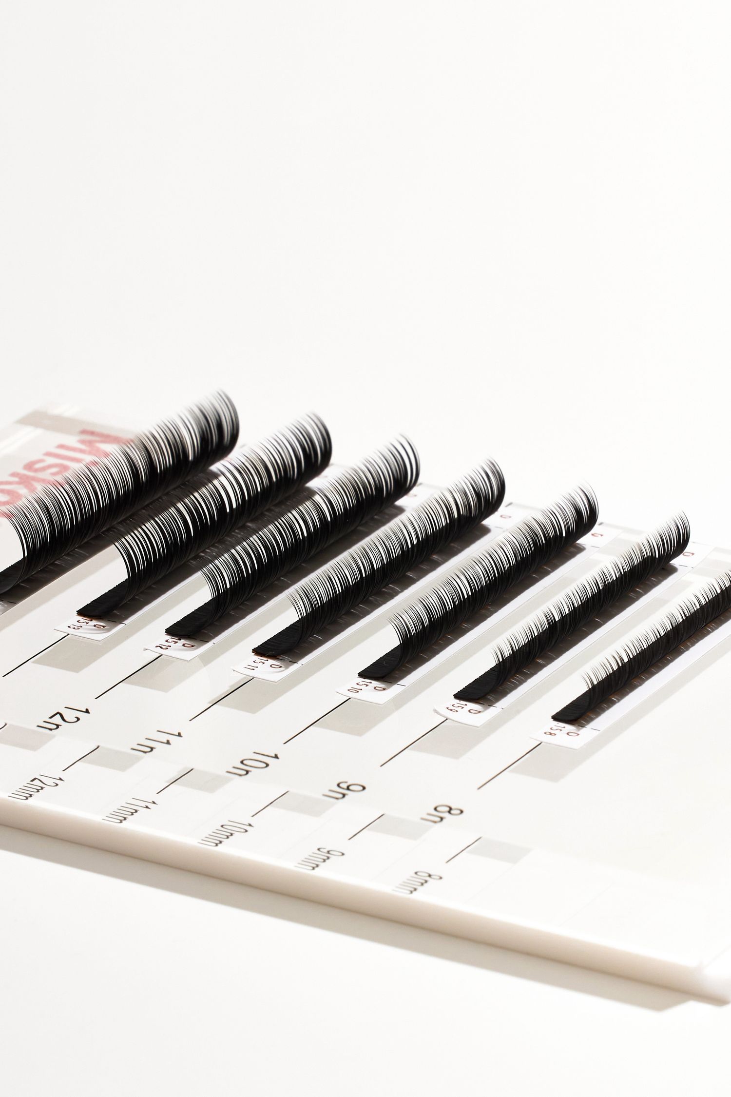 Professional eyelash extension strips arranged in ascending length on white display.