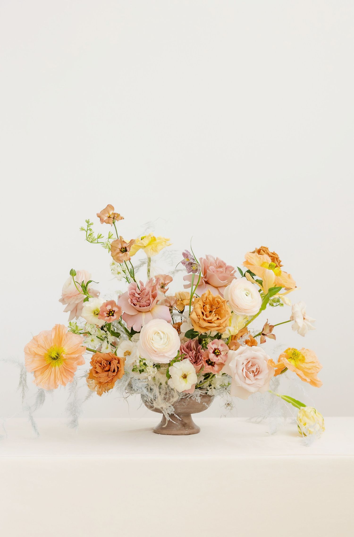 Elegant floral arrangement with peach, pink and yellow blooms in soft pastel tones against white background.