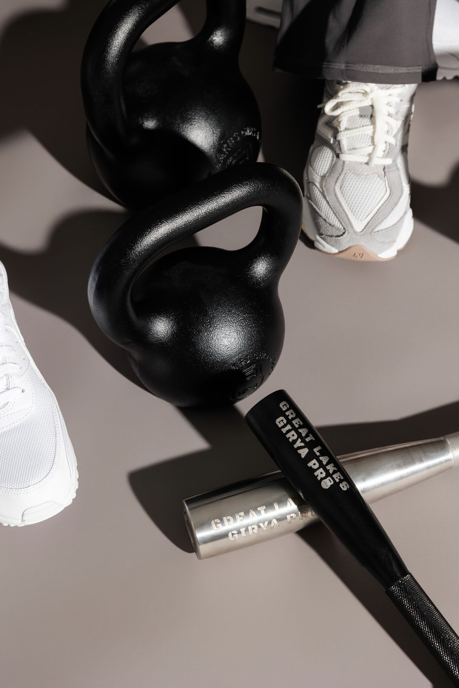 Two black kettlebells and white sneakers arranged with fitness equipment on gray background.