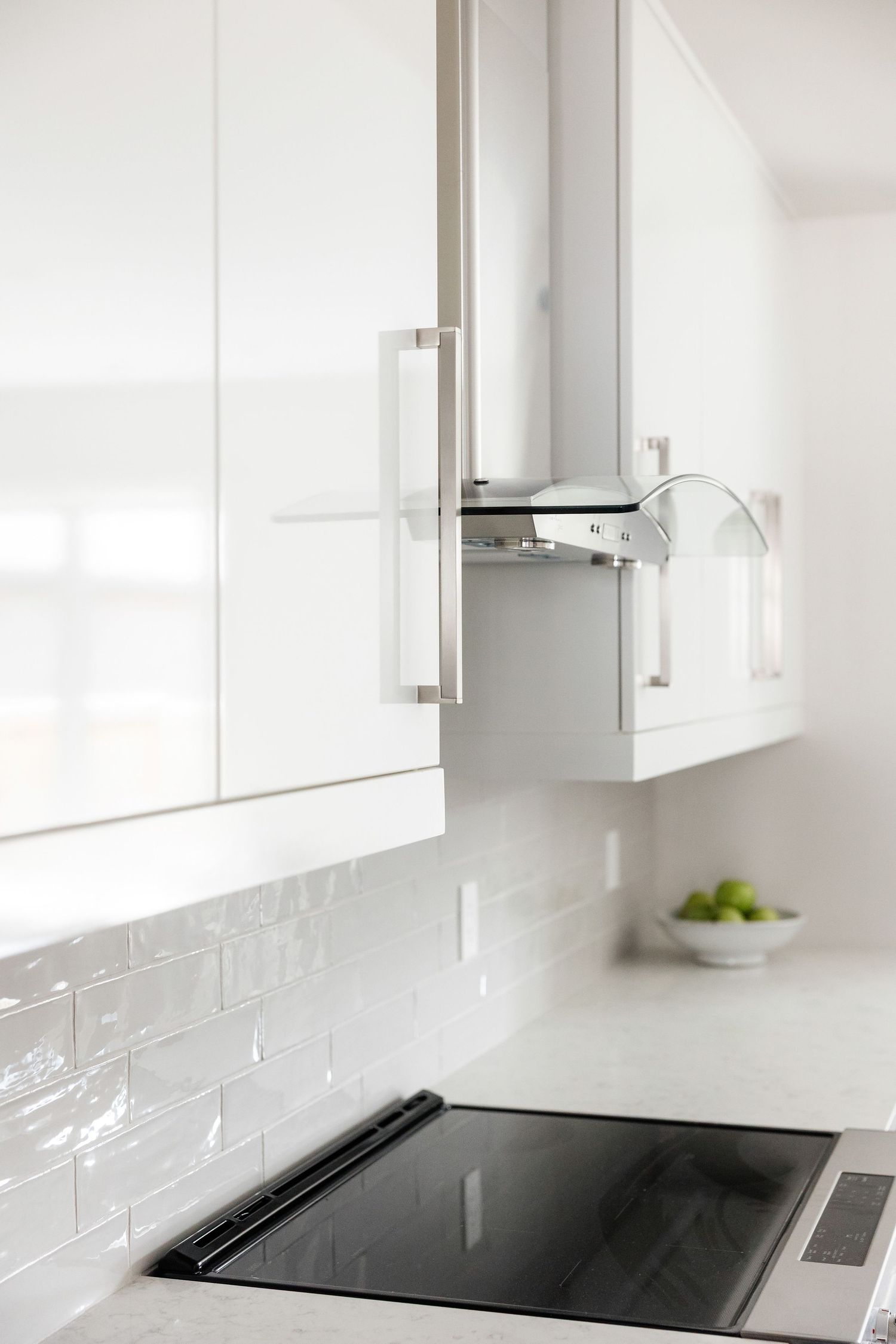 Modern white kitchen cabinets with sleek black cooktop and subway tile backsplash.