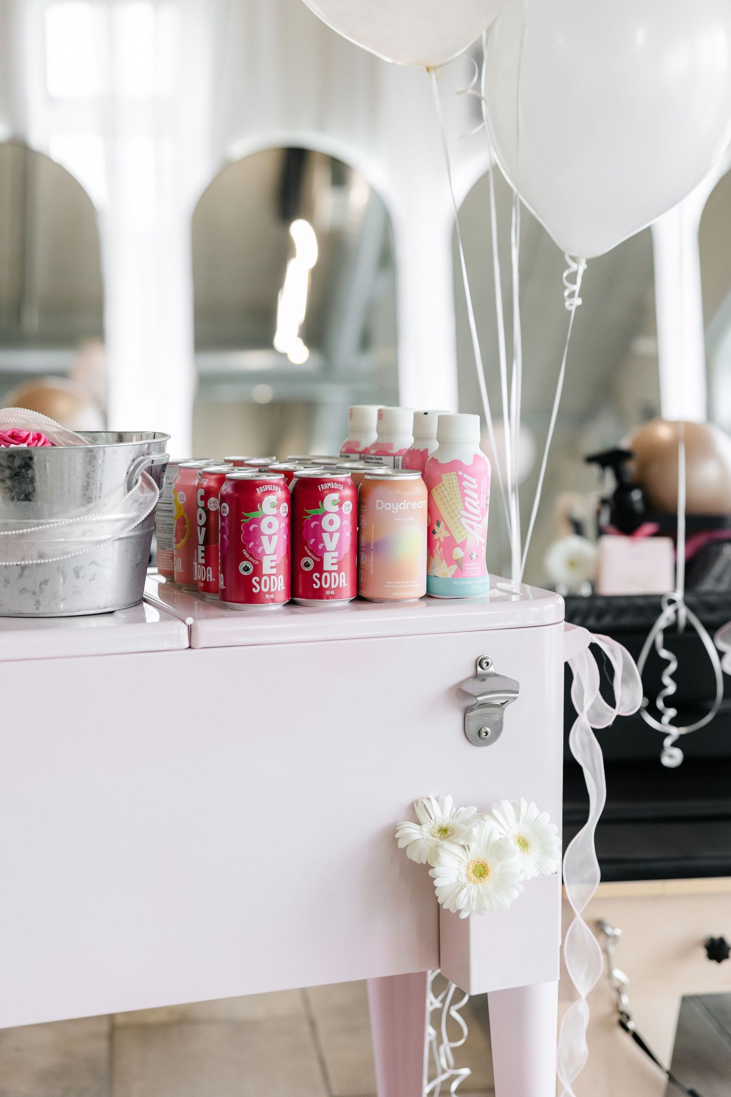 White fitness studio counter with pink beverages and white balloons on display.