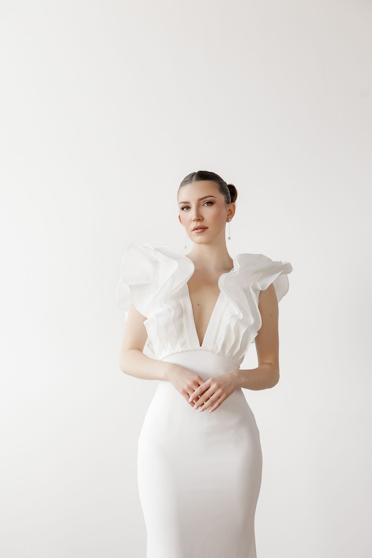 Modern wedding dress with dramatic ruffled shoulders in sleek minimalist design.