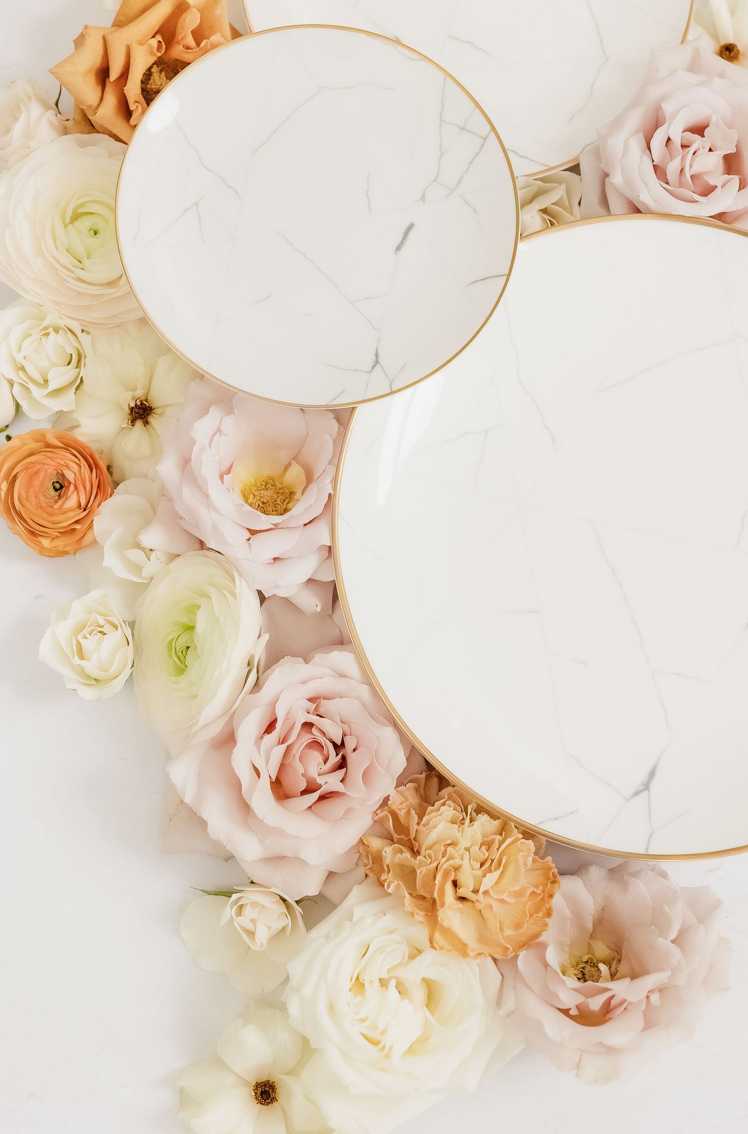 Elegant white marble plates surrounded by blush pink and cream roses on a light background.