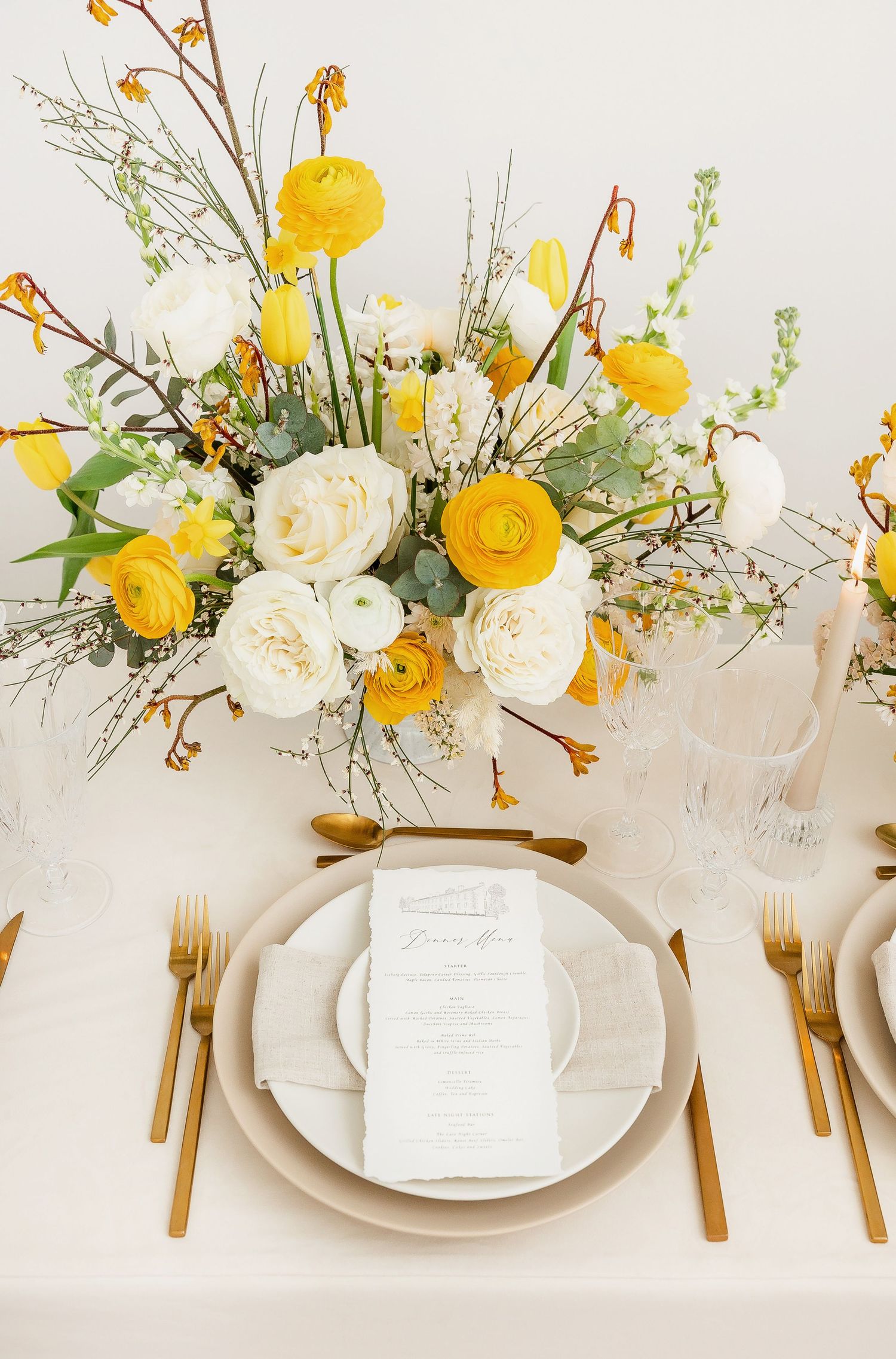 Wedding table setting with yellow and white floral centerpiece and gold flatware.